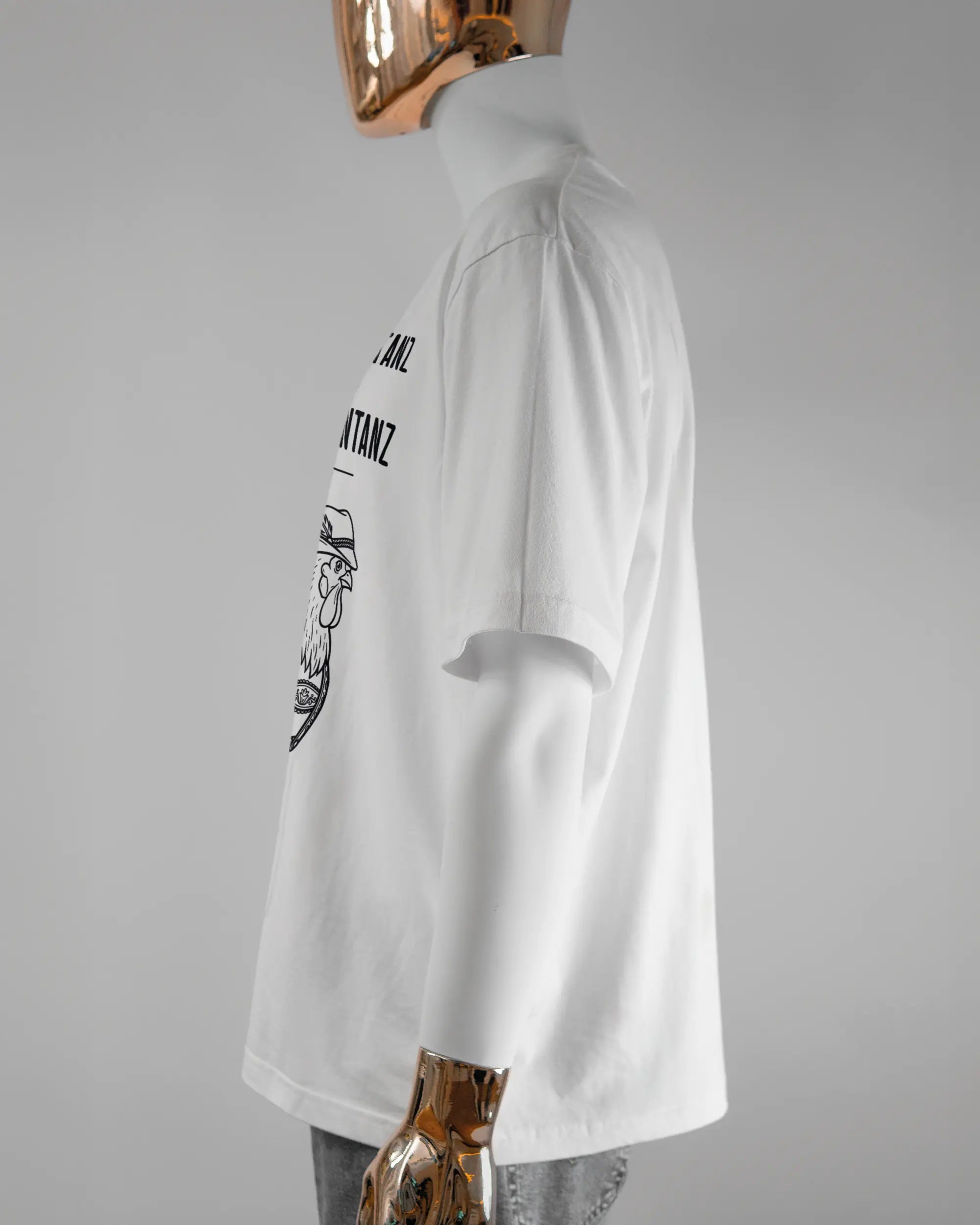 Seitenansicht des Basic Unisex T-Shirt Oversized von Maondo mit dem Design Trachtentanz vorne in der Farbe White und in der Größe L getragen von einer maskulinen Puppe