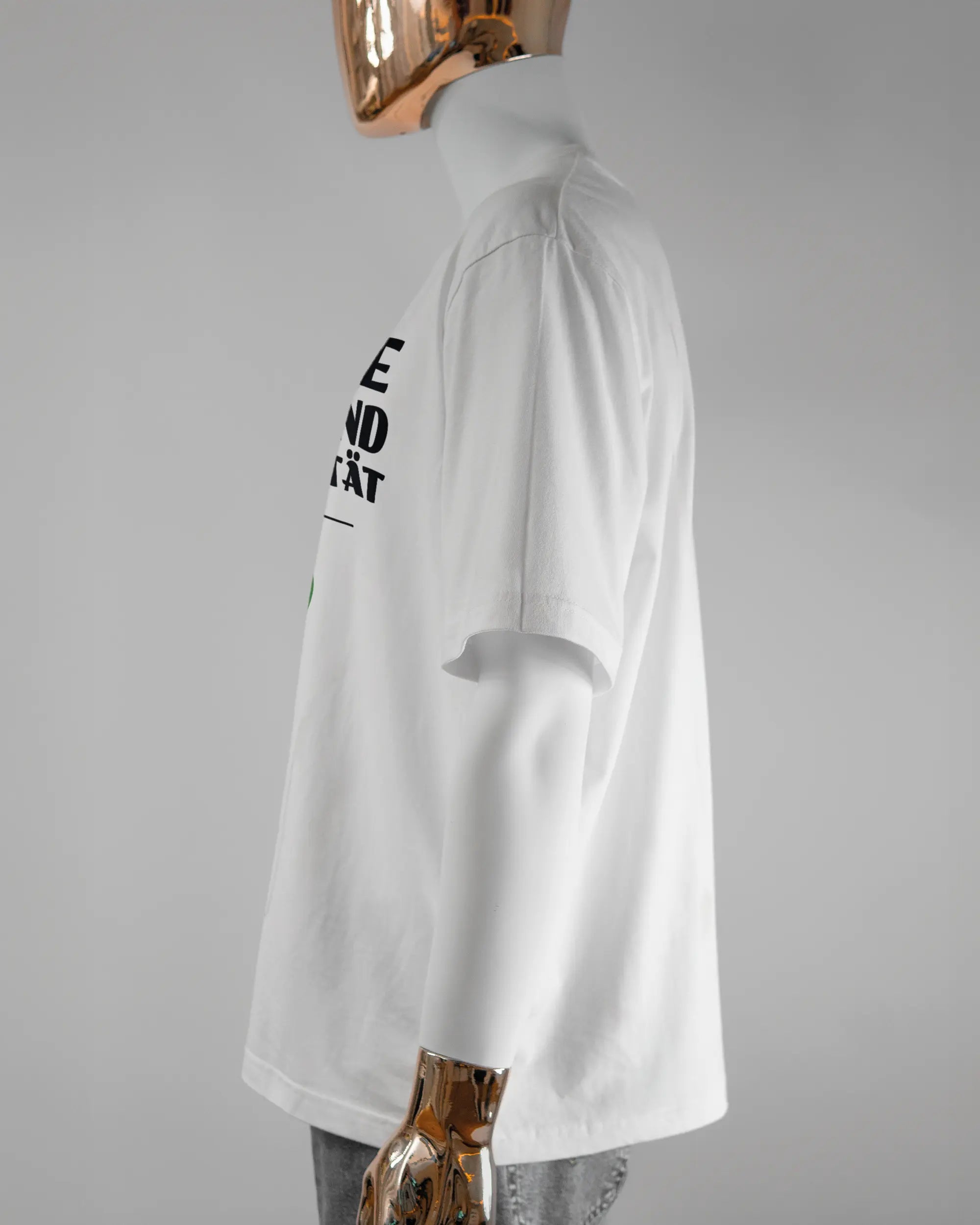 Seitenansicht des Basic Unisex T-Shirt Oversized von Maondo mit dem Design Keine Eile vorne in der Farbe White und in der Größe L getragen von einer maskulinen Puppe