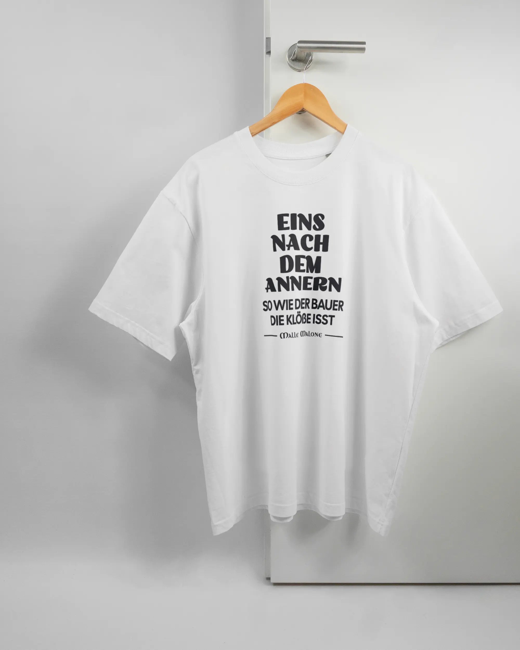 Vorderseite des Basic Unisex T-Shirt Oversized von Maondo mit dem Design Eins nach dem Annern in der Farbe White und in der Größe L auf einem Bügel an der Türklinke aufgehängt