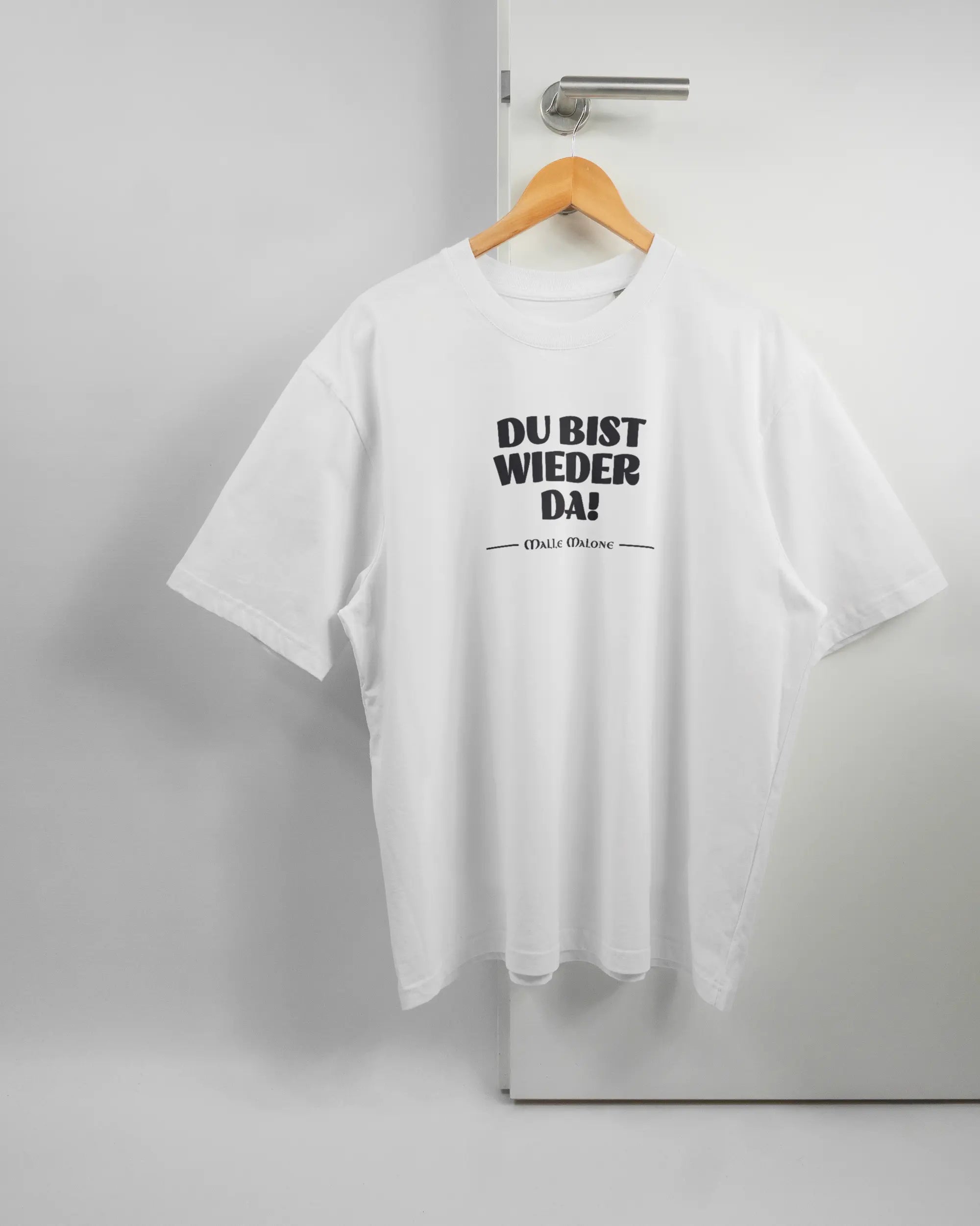 Vorderseite des Basic Unisex T-Shirt Oversized von Maondo mit dem Design Wieder da in der Farbe White und in der Größe L auf einem Bügel an der Türklinke aufgehängt