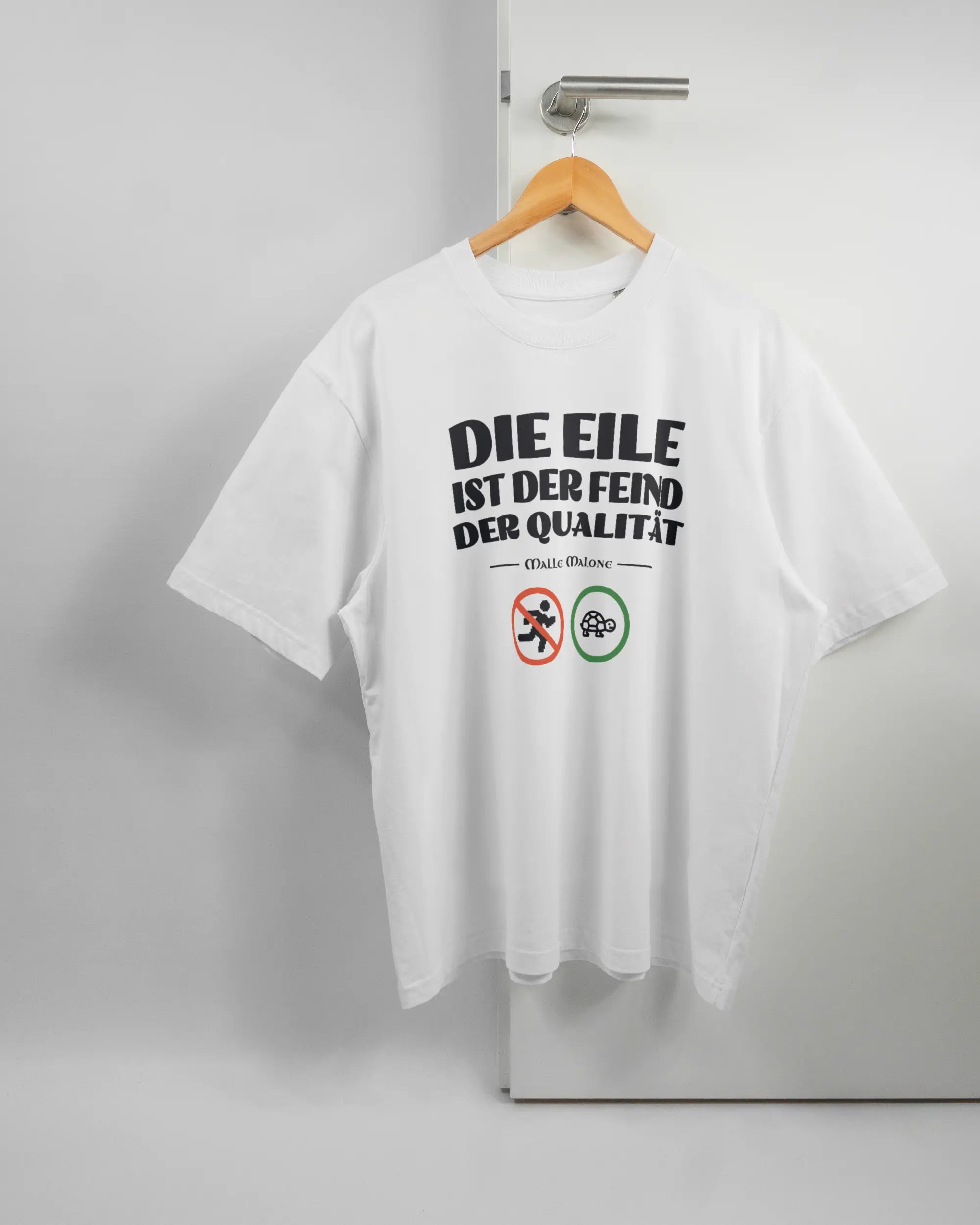 Vorderseite des Basic Unisex T-Shirt Oversized von Maondo mit dem Design Keine Eile in der Farbe White und in der Größe L auf einem Bügel an der Türklinke aufgehängt