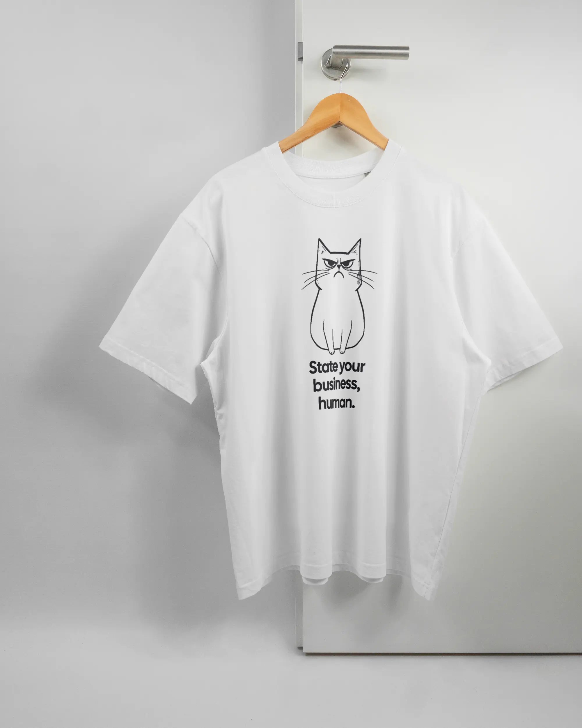 Vorderseite des Basic Unisex T-Shirt Oversized von Maondo mit dem Design Grumpy Purr in der Farbe White und in der Größe L auf einem Bügel an der Türklinke aufgehängt
