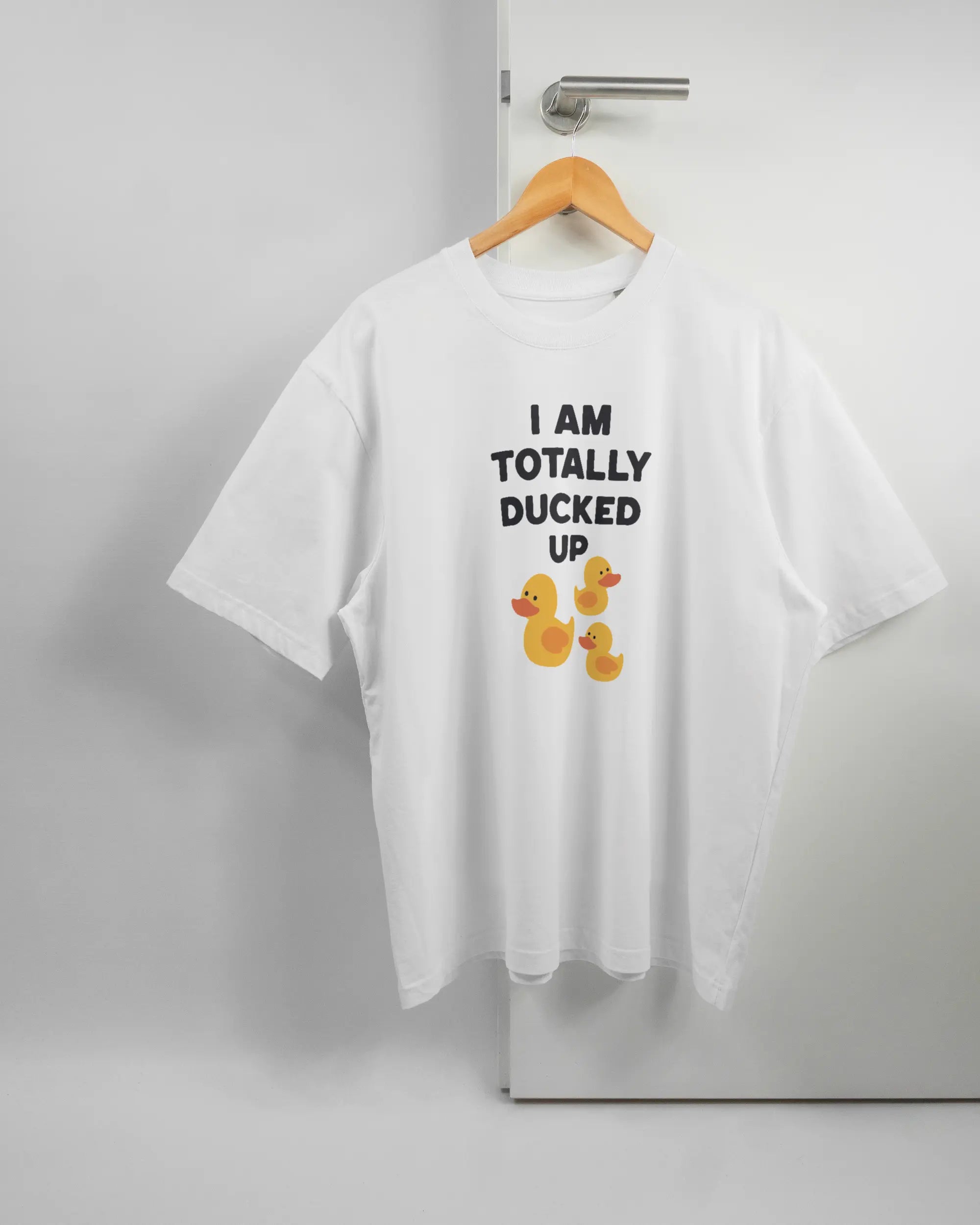Vorderseite des Basic Unisex T-Shirt Oversized von Maondo mit dem Design Ducked Up in der Farbe White und in der Größe L auf einem Bügel an der Türklinke aufgehängt