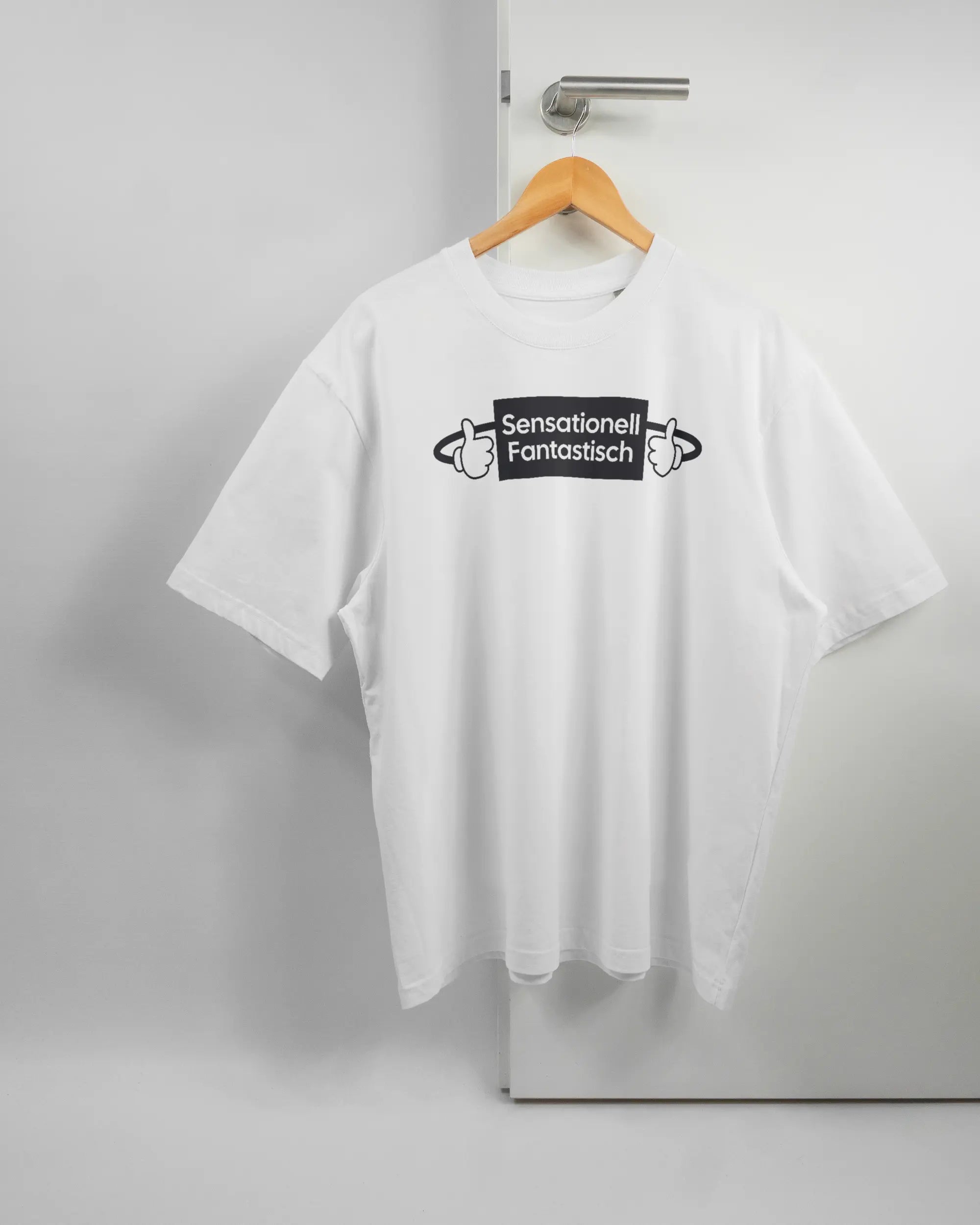 Vorderseite des Basic Unisex T-Shirt Oversized von Maondo mit dem Design Fantastisch in der Farbe White und in der Größe L auf einem Bügel an der Türklinke aufgehängt