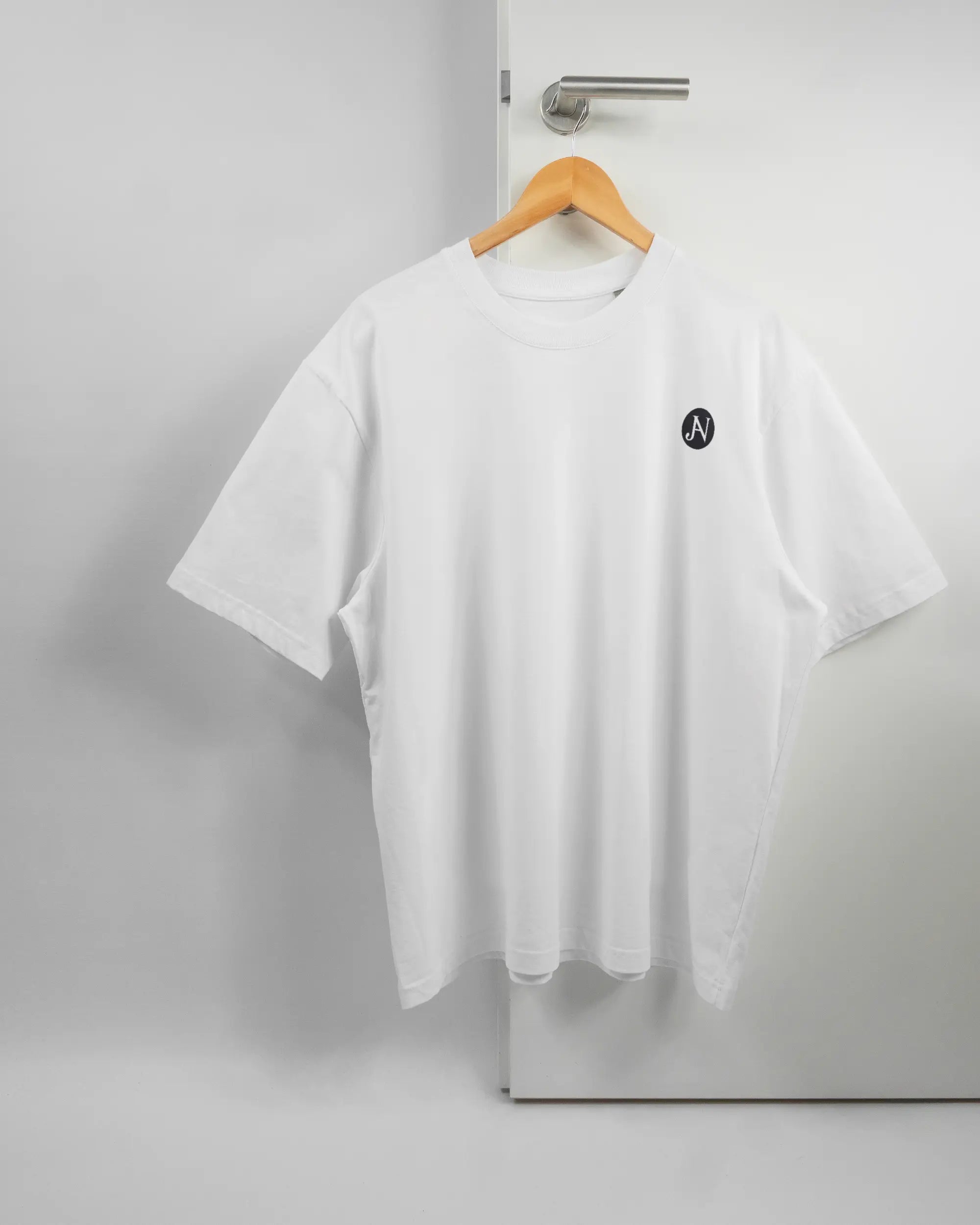Vorderseite des Basic Unisex T-Shirt Oversized von Maondo mit dem Design JB1 in der Farbe White und in der Größe L auf einem Bügel an der Türklinke aufgehängt