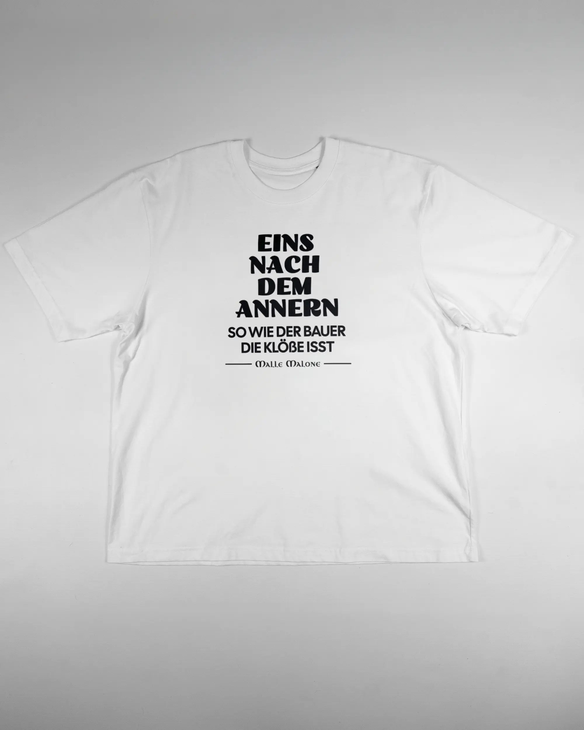 Vorderseite des Basic Unisex T-Shirt Oversized von Maondo mit dem Design Eins nach dem Annern in der Farbe White und in der Größe L flach auf den Boden gelegt