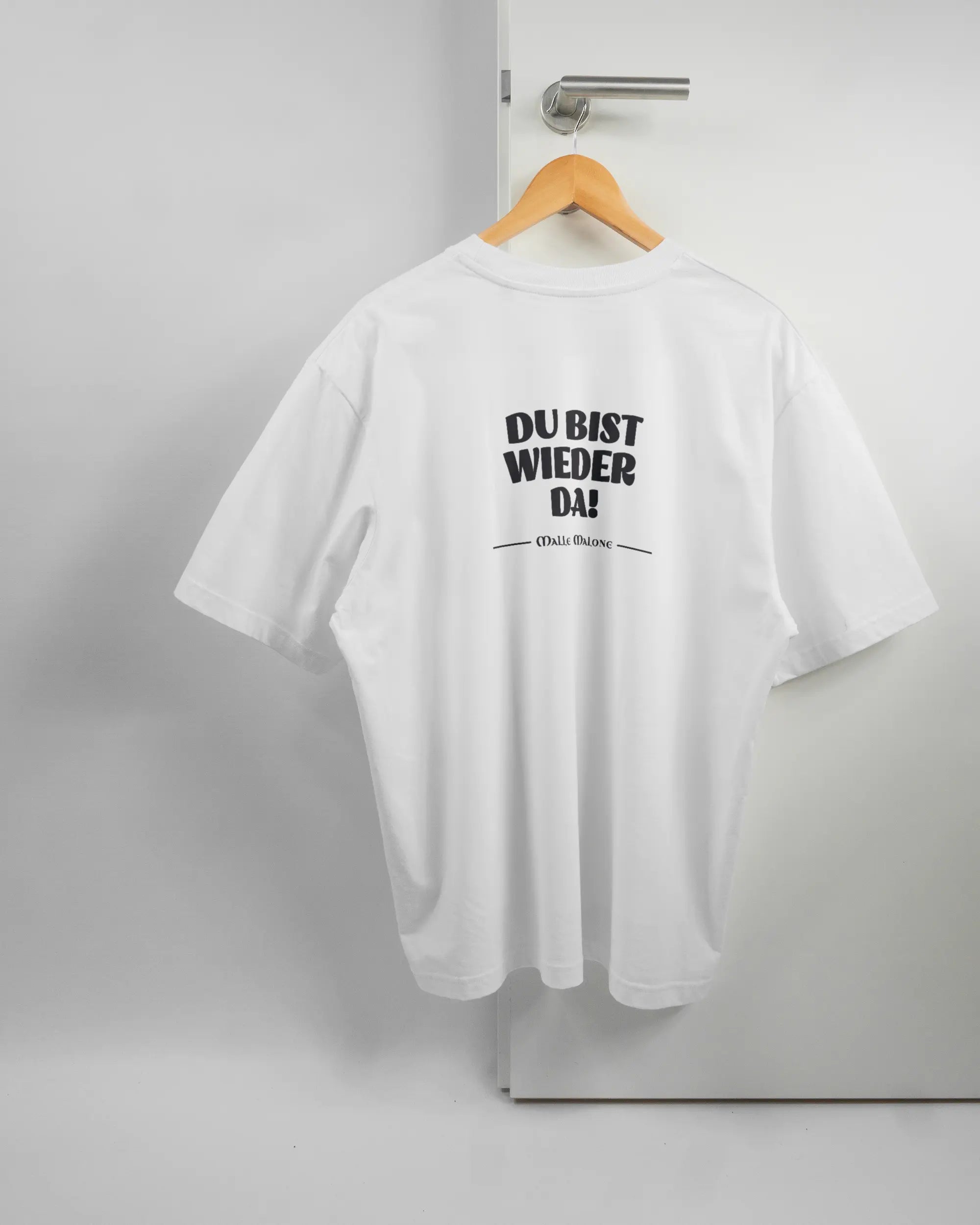 Rückseite des Basic Unisex T-Shirt Oversized von Maondo mit dem Design Wieder da in der Farbe White und in der Größe L auf einem Bügel an der Türklinke aufgehängt