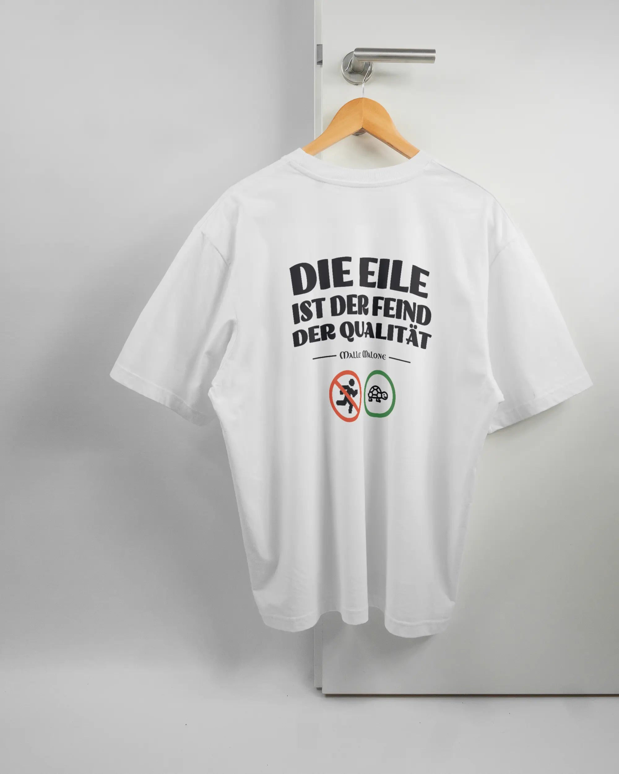Rückseite des Basic Unisex T-Shirt Oversized von Maondo mit dem Design Keine Eile in der Farbe White und in der Größe L auf einem Bügel an der Türklinke aufgehängt