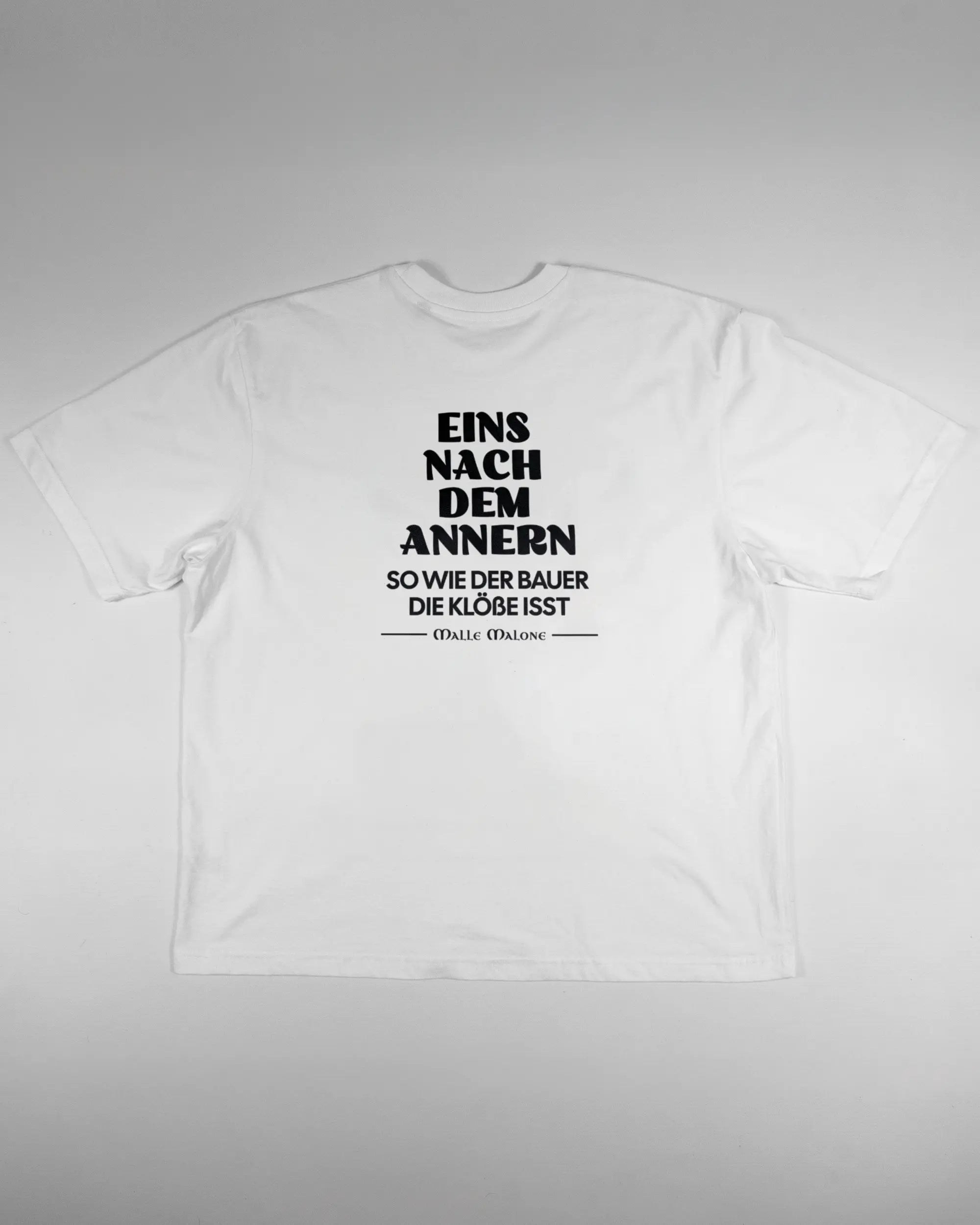 Rückseite des Basic Unisex T-Shirt Oversized von Maondo mit dem Design Eins nach dem Annern in der Farbe White und in der Größe L flach auf den Boden gelegt