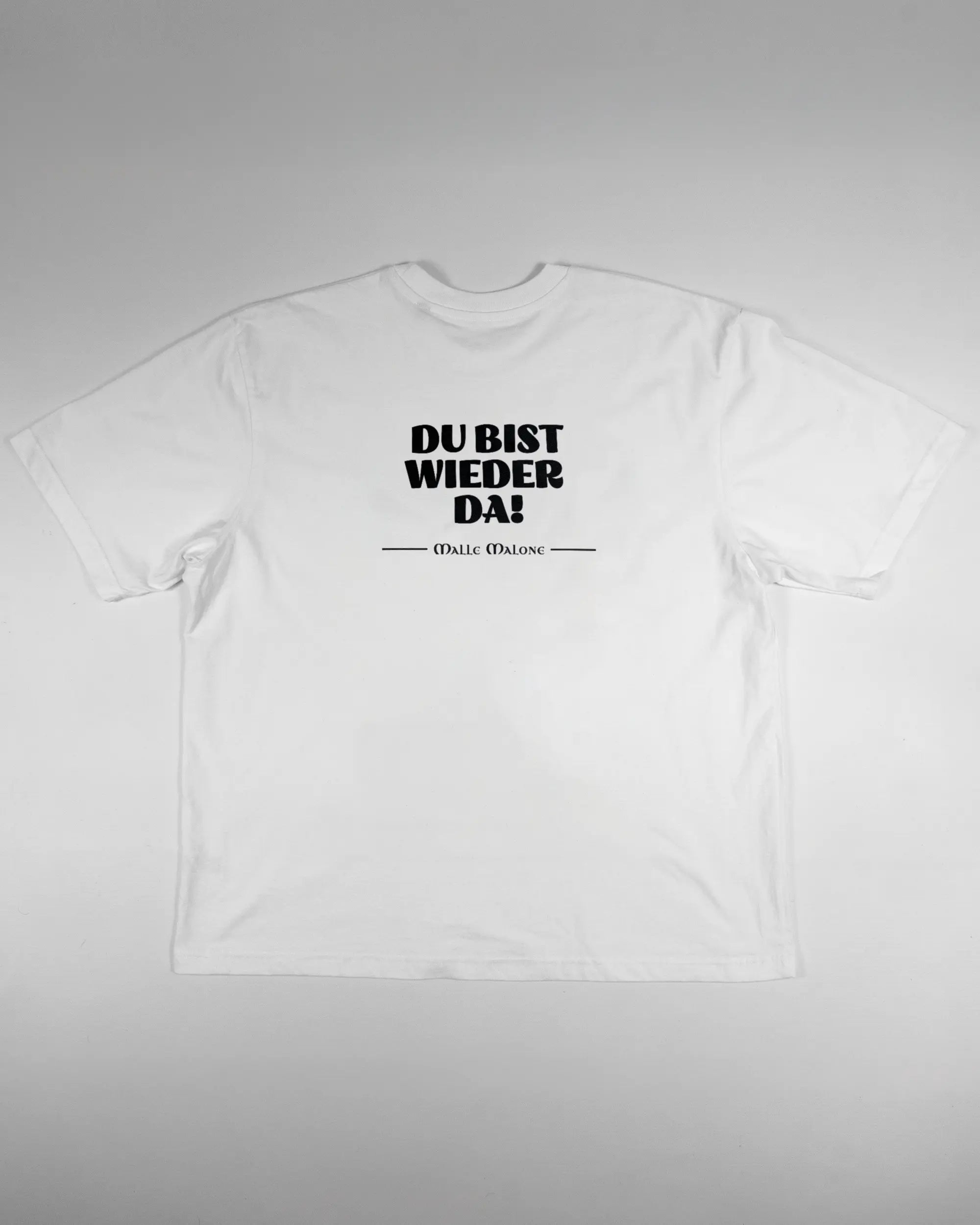 Rückseite des Basic Unisex T-Shirt Oversized von Maondo mit dem Design Wieder da in der Farbe White und in der Größe L flach auf den Boden gelegt