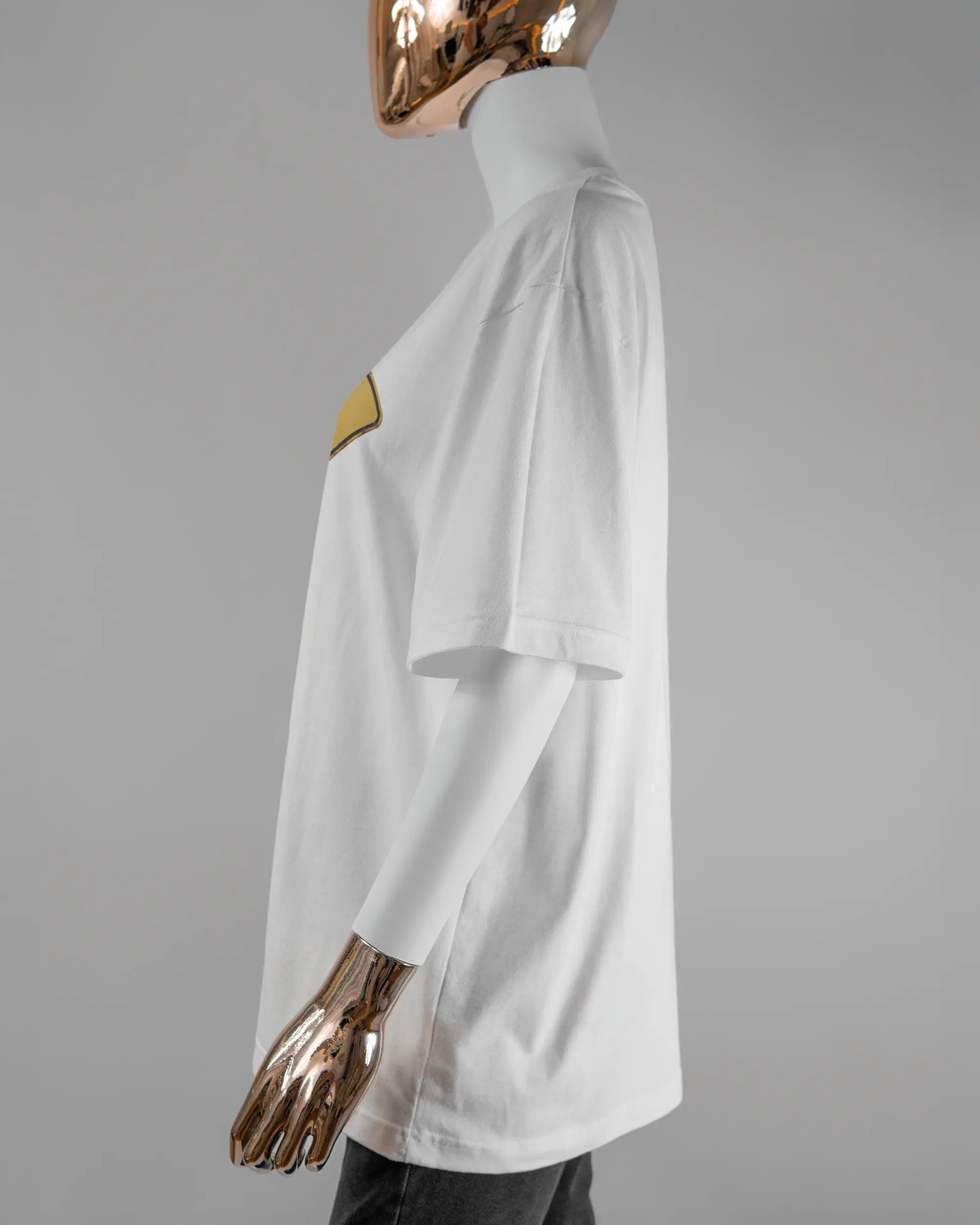 Seitenansicht des Basic Unisex T-Shirt Oversized von Maondo mit dem Design Schutzschild vorne in der Farbe White und in der Größe S getragen von einer femininen Puppe