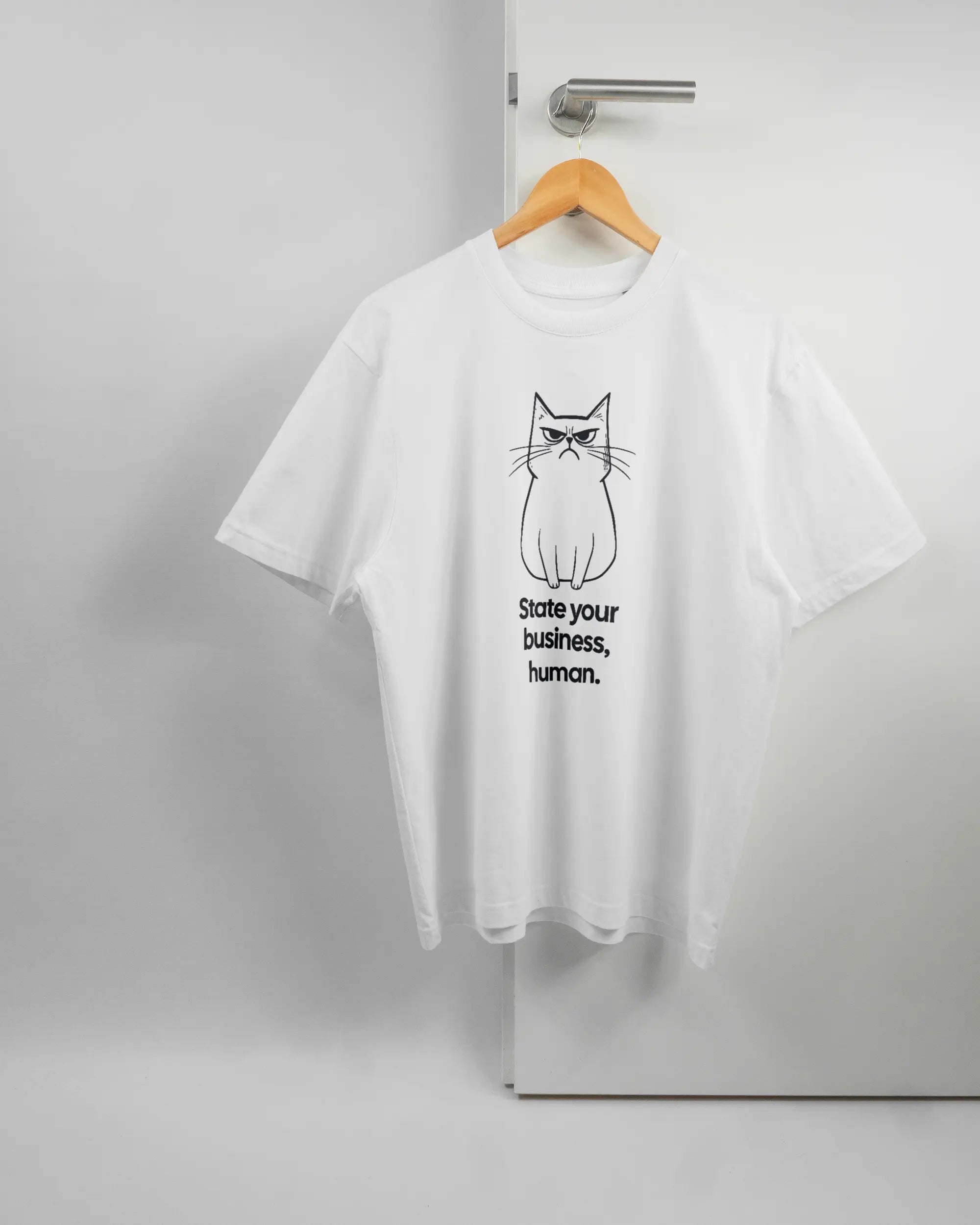 Vorderseite des Basic Unisex T-Shirt Oversized von Maondo mit dem Design Grumpy Purr in der Farbe White und in der Größe S auf einem Bügel an der Türklinke aufgehängt
