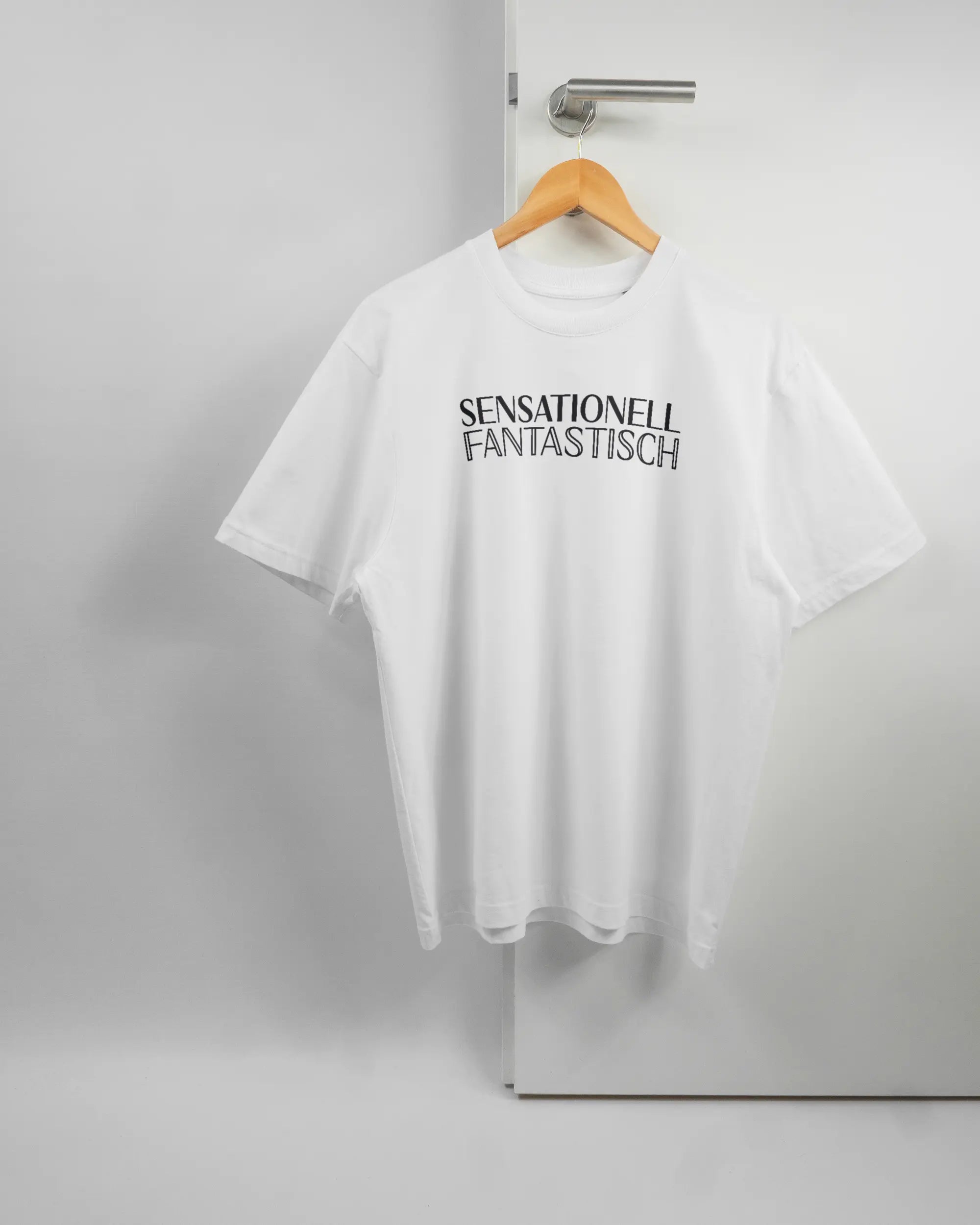 Vorderseite des Basic Unisex T-Shirt Oversized von Maondo mit dem Design Sensationell in der Farbe White und in der Größe S auf einem Bügel an der Türklinke aufgehängt