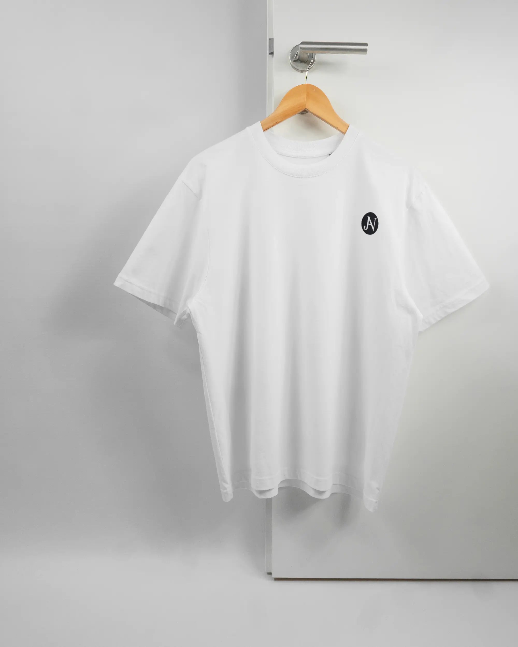 Vorderseite des Basic Unisex T-Shirt Oversized von Maondo mit dem Design JB1 in der Farbe White und in der Größe S auf einem Bügel an der Türklinke aufgehängt