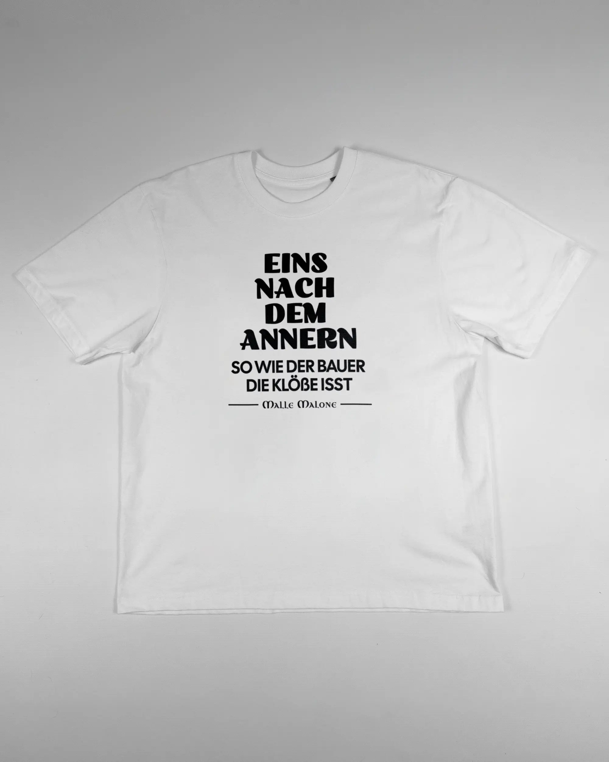 Vorderseite des Basic Unisex T-Shirt Oversized von Maondo mit dem Design Eins nach dem Annern in der Farbe White und in der Größe S flach auf den Boden gelegt