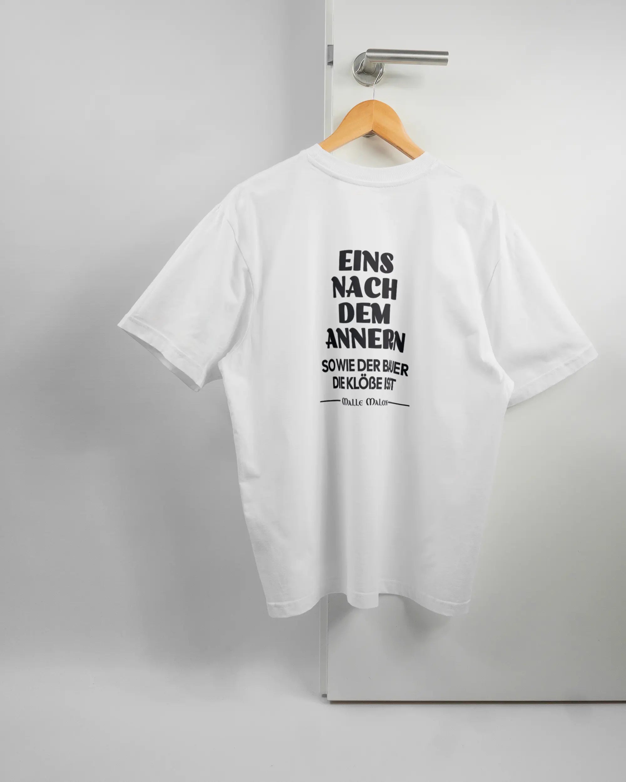 Rückseite des Basic Unisex T-Shirt Oversized von Maondo mit dem Design Eins nach dem Annern in der Farbe White und in der Größe S auf einem Bügel an der Türklinke aufgehängt