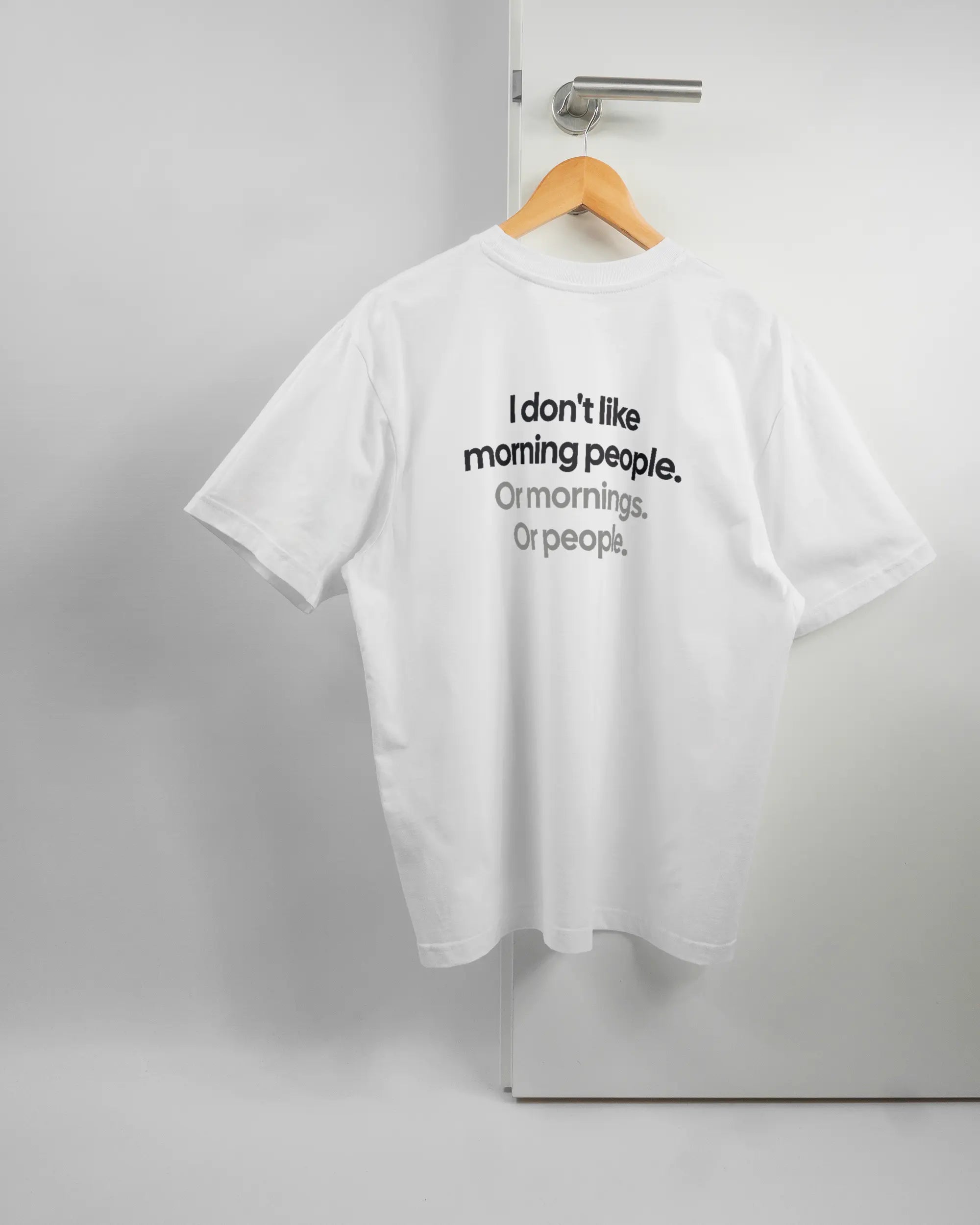 Rückseite des Basic Unisex T-Shirt Oversized von Maondo mit dem Design Morning Person in der Farbe White und in der Größe S auf einem Bügel an der Türklinke aufgehängt