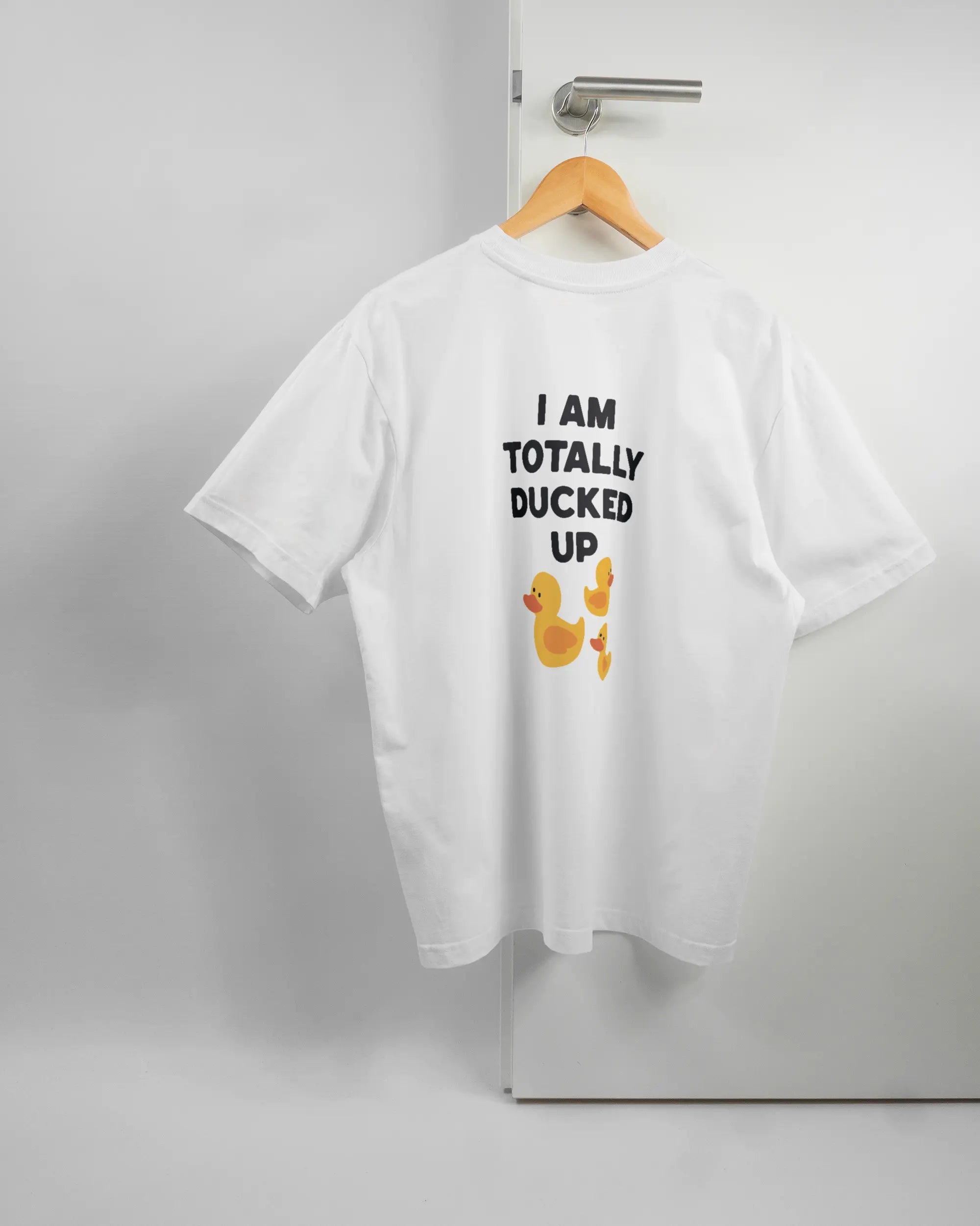 Rückseite des Basic Unisex T-Shirt Oversized von Maondo mit dem Design Ducked Up in der Farbe White und in der Größe S auf einem Bügel an der Türklinke aufgehängt