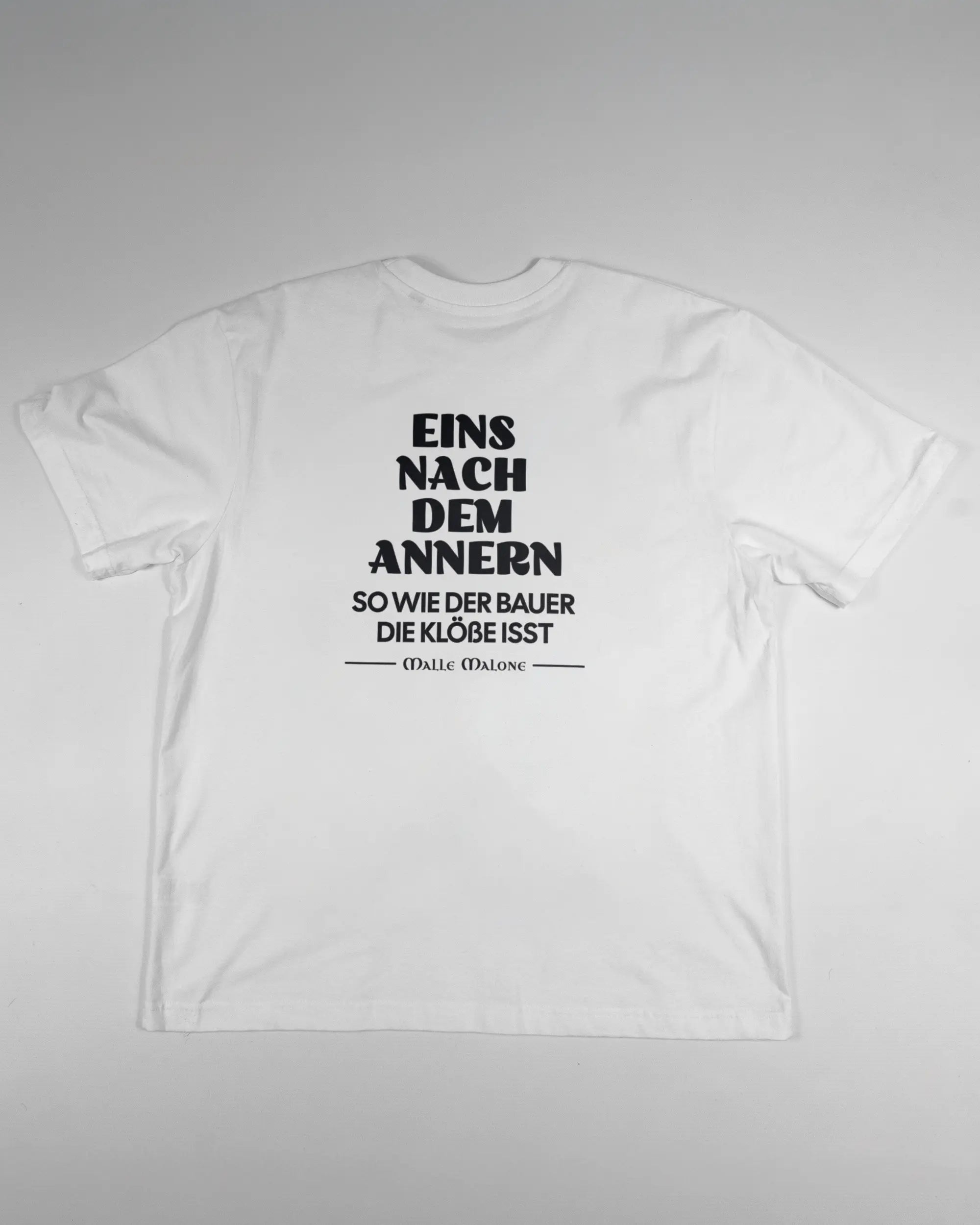Rückseite des Basic Unisex T-Shirt Oversized von Maondo mit dem Design Eins nach dem Annern in der Farbe White und in der Größe S flach auf den Boden gelegt