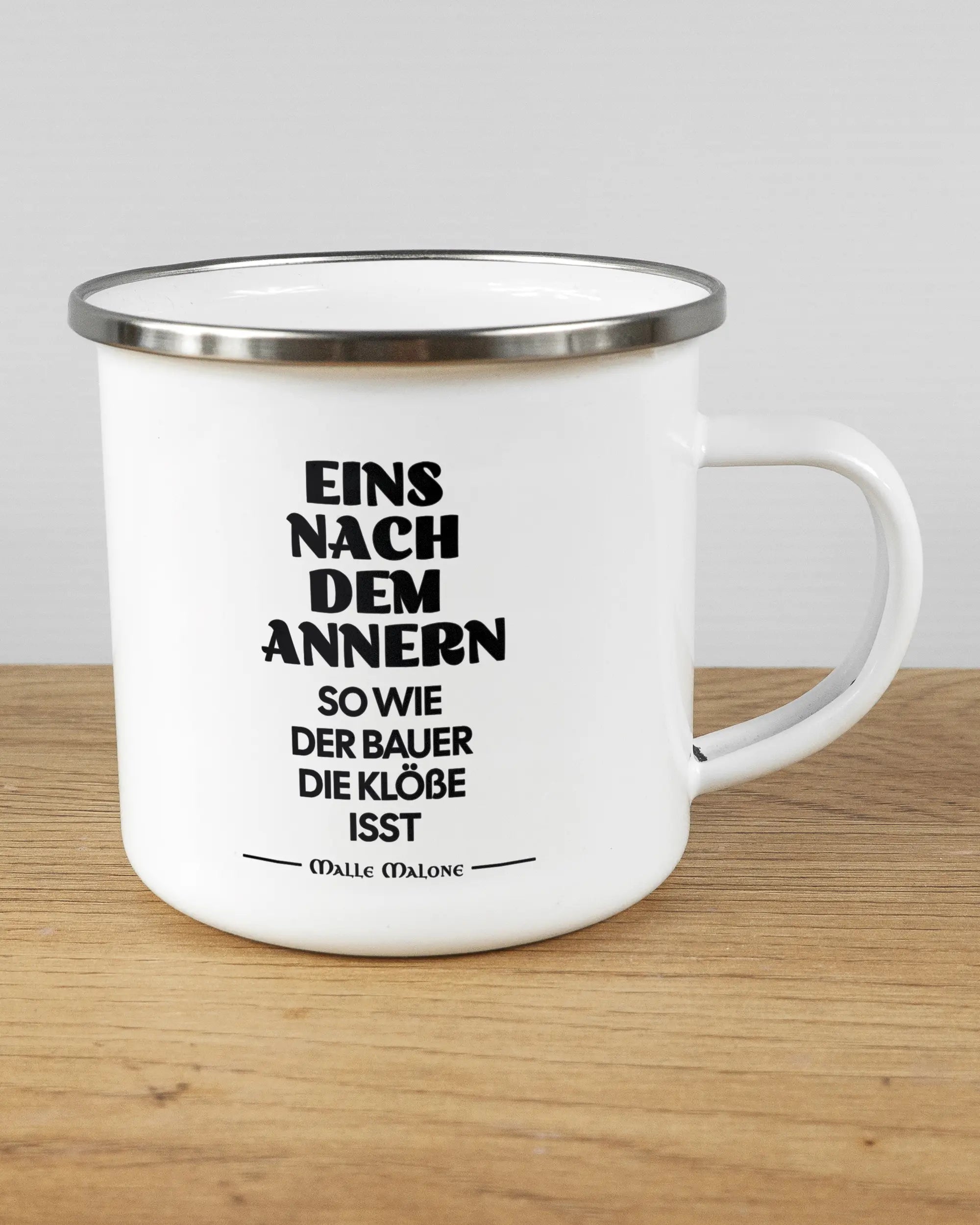 Alternativbild, das die rechte Seite der beidseitig bedruckten Emailletasse von Maondo mit dem Design Eins nach dem Annern in der Farbe White-Silver auf einem Holztisch zeigt