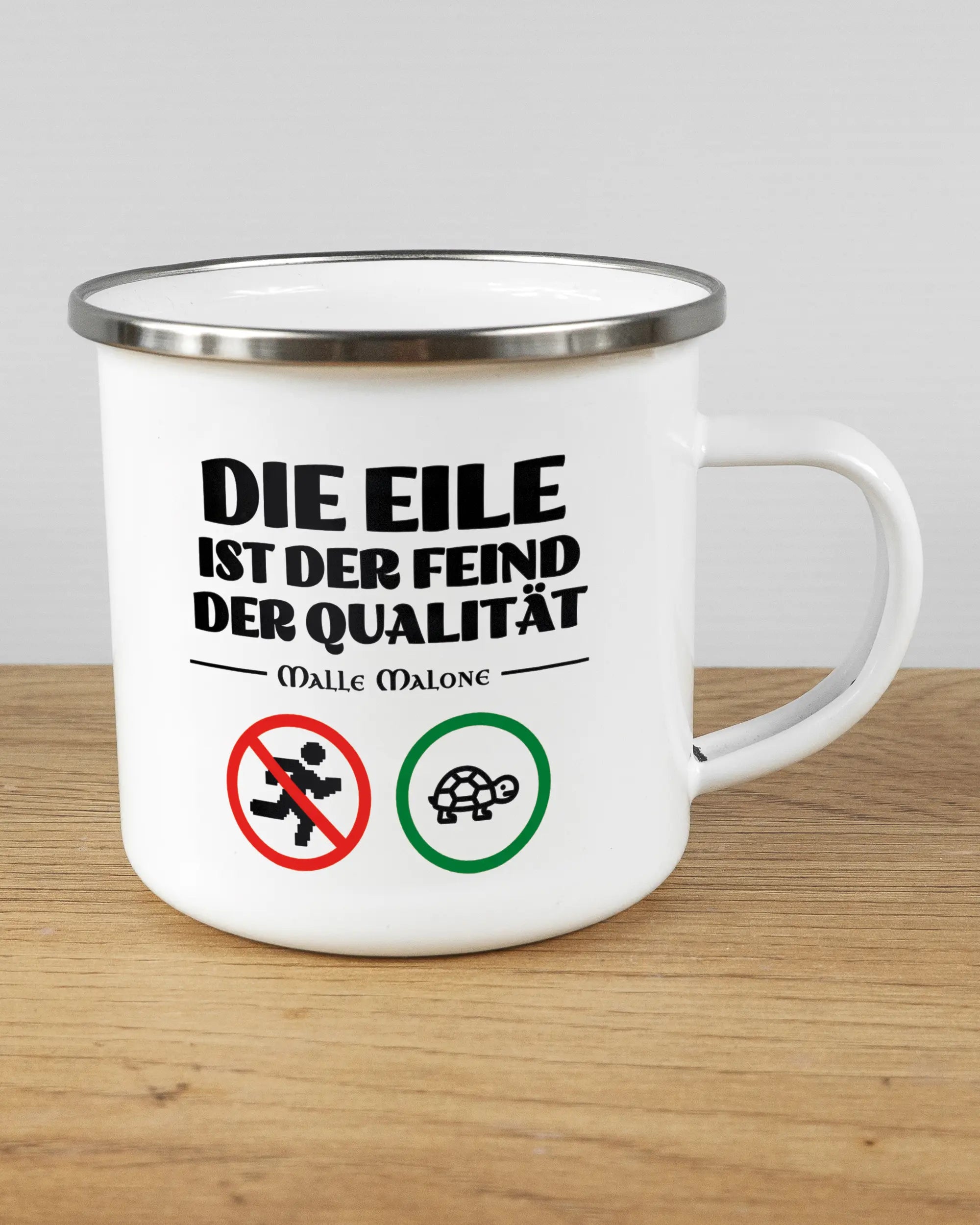 Alternativbild, das die rechte Seite der beidseitig bedruckten Emailletasse von Maondo mit dem Design Keine Eile in der Farbe White-Silver auf einem Holztisch zeigt