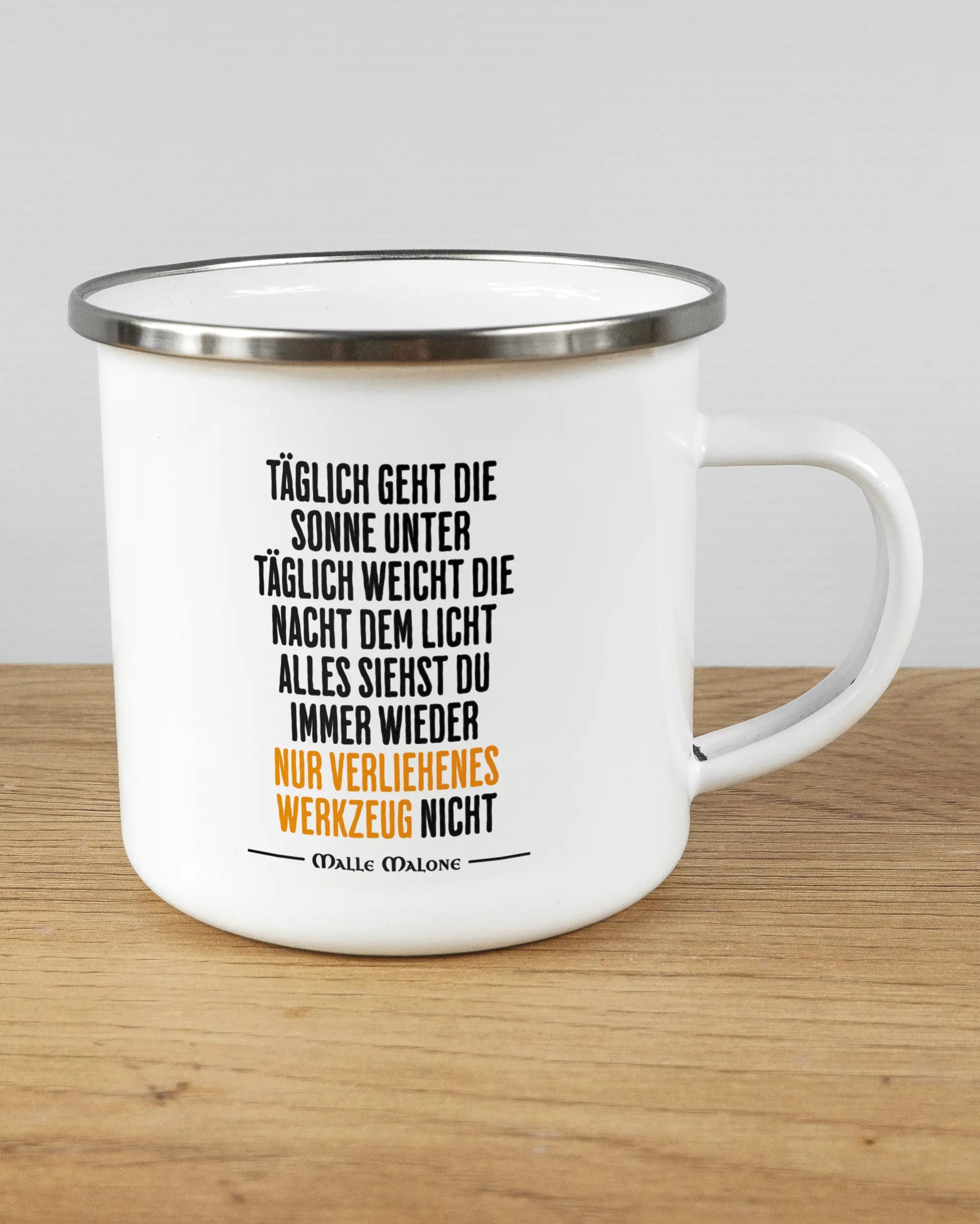 Alternativbild, das die rechte Seite der beidseitig bedruckten Emailletasse von Maondo mit dem Design Wegzeug in der Farbe White-Silver auf einem Holztisch zeigt
