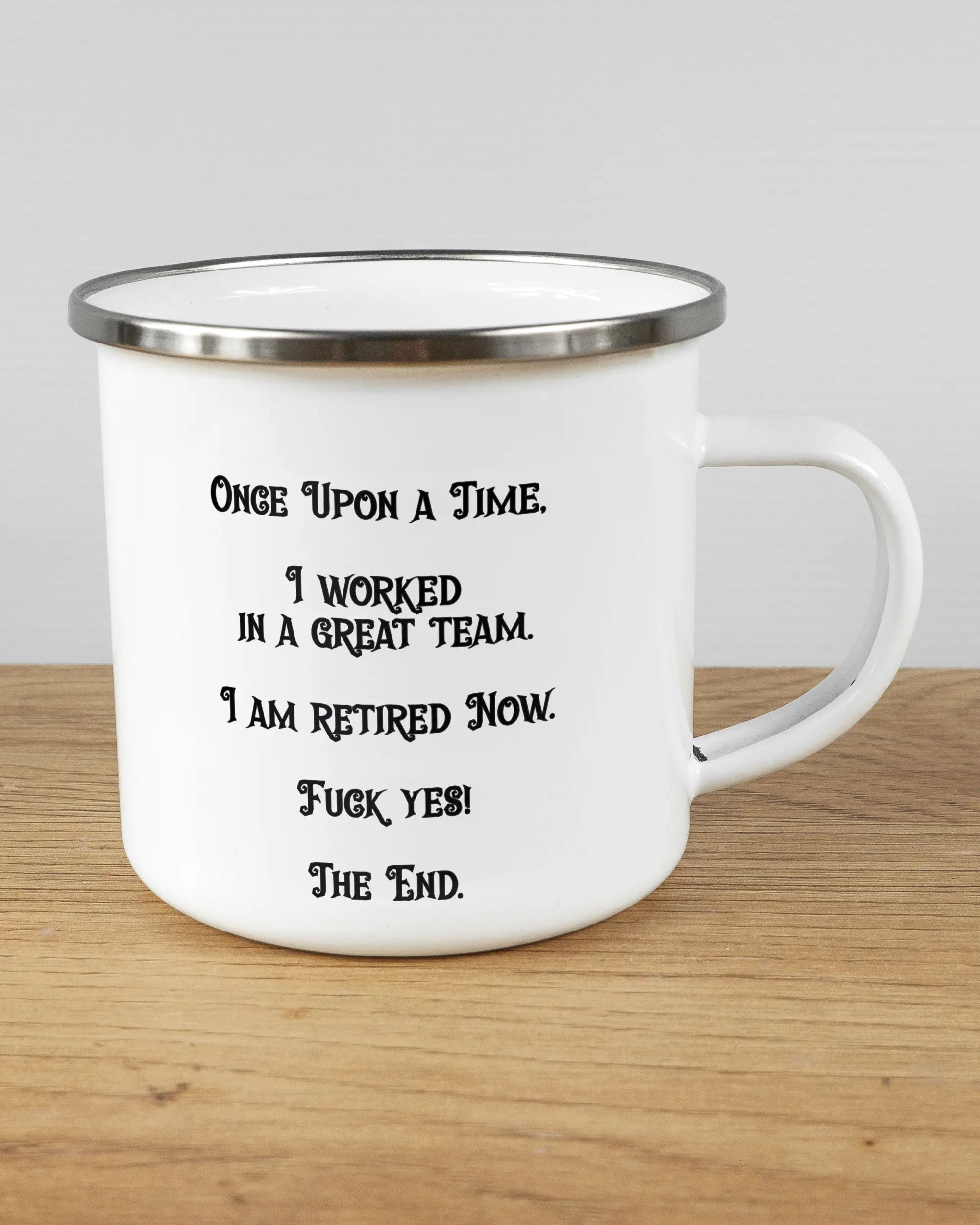 Alternativbild, das die rechte Seite der beidseitig bedruckten Emailletasse von Maondo mit dem Design Finally Retired in der Farbe White-Silver auf einem Holztisch zeigt