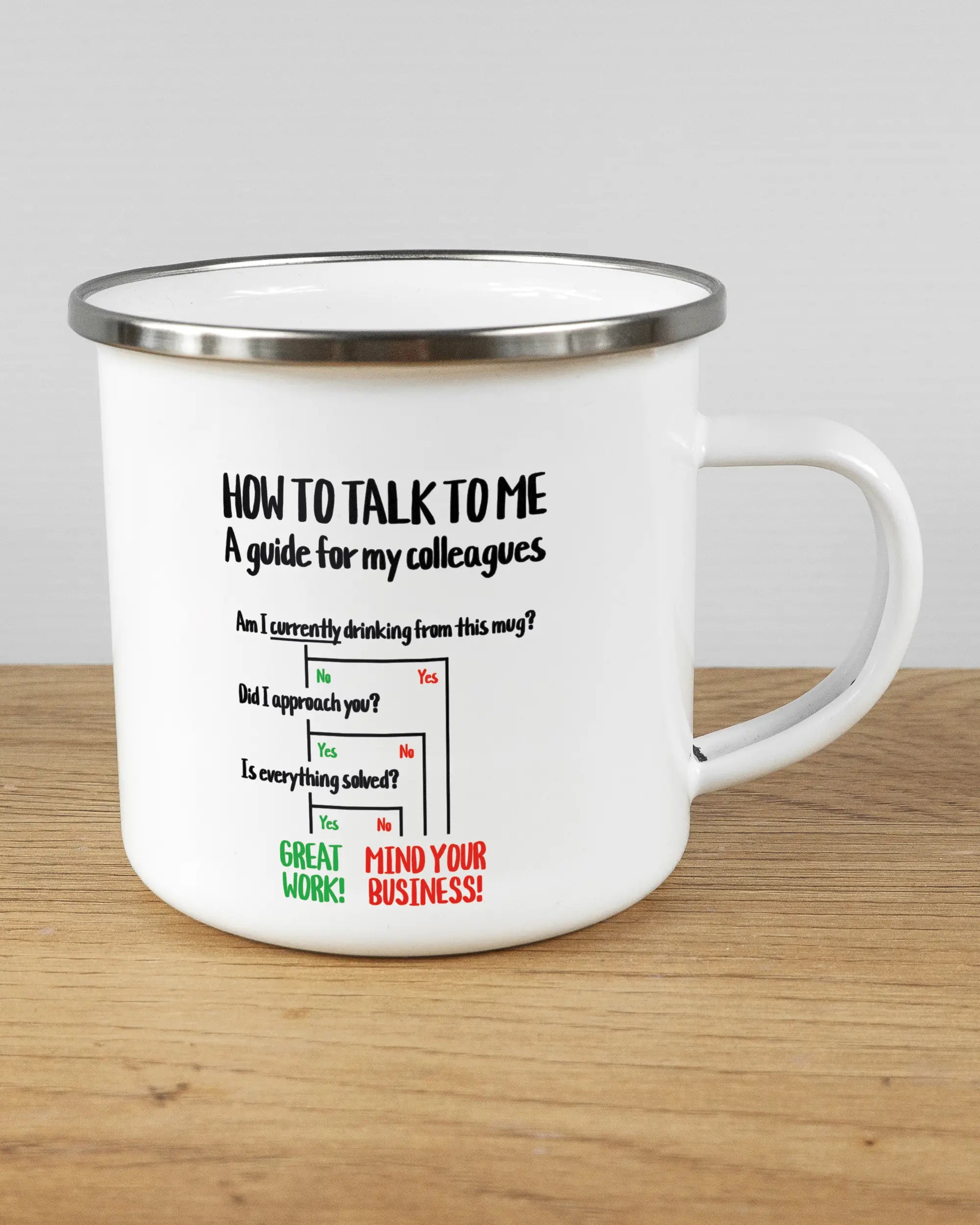 Alternativbild, das die rechte Seite der beidseitig bedruckten Emailletasse von Maondo mit dem Design Colleagues Guide in der Farbe White-Silver auf einem Holztisch zeigt