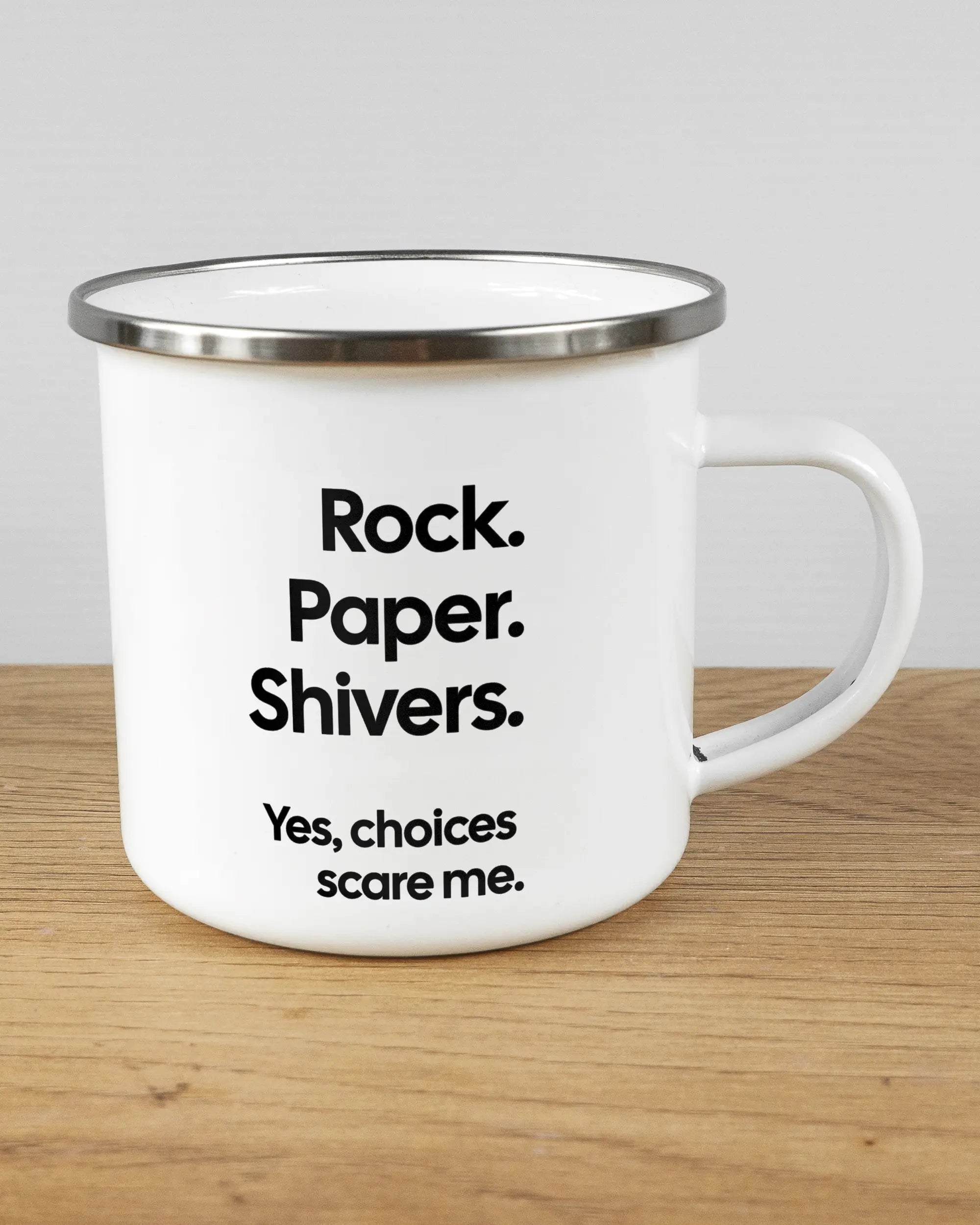 Alternativbild, das die rechte Seite der beidseitig bedruckten Emailletasse von Maondo mit dem Design Rock Paper Shivers in der Farbe White-Silver auf einem Holztisch zeigt