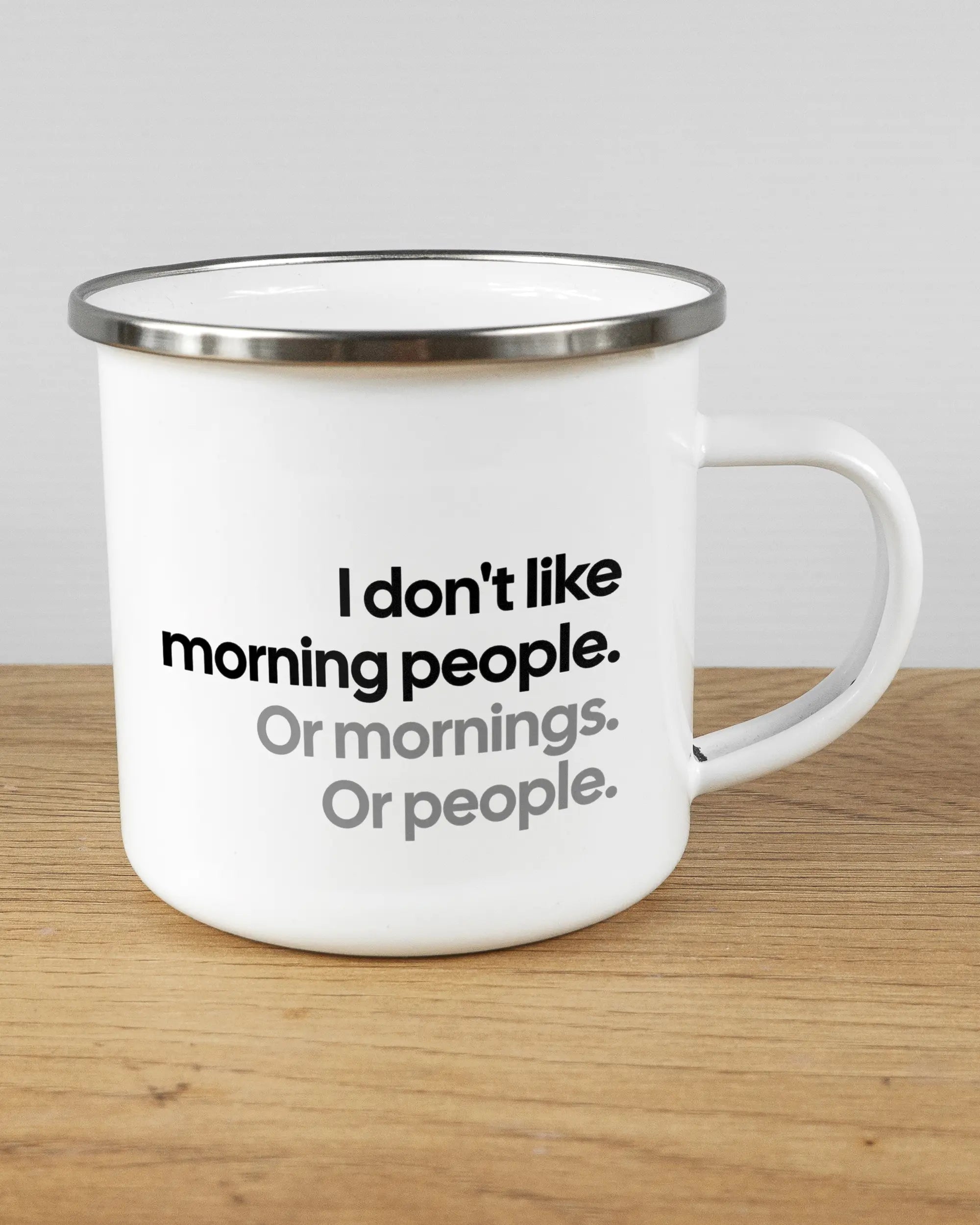 Alternativbild, das die rechte Seite der beidseitig bedruckten Emailletasse von Maondo mit dem Design Morning Person in der Farbe White-Silver auf einem Holztisch zeigt