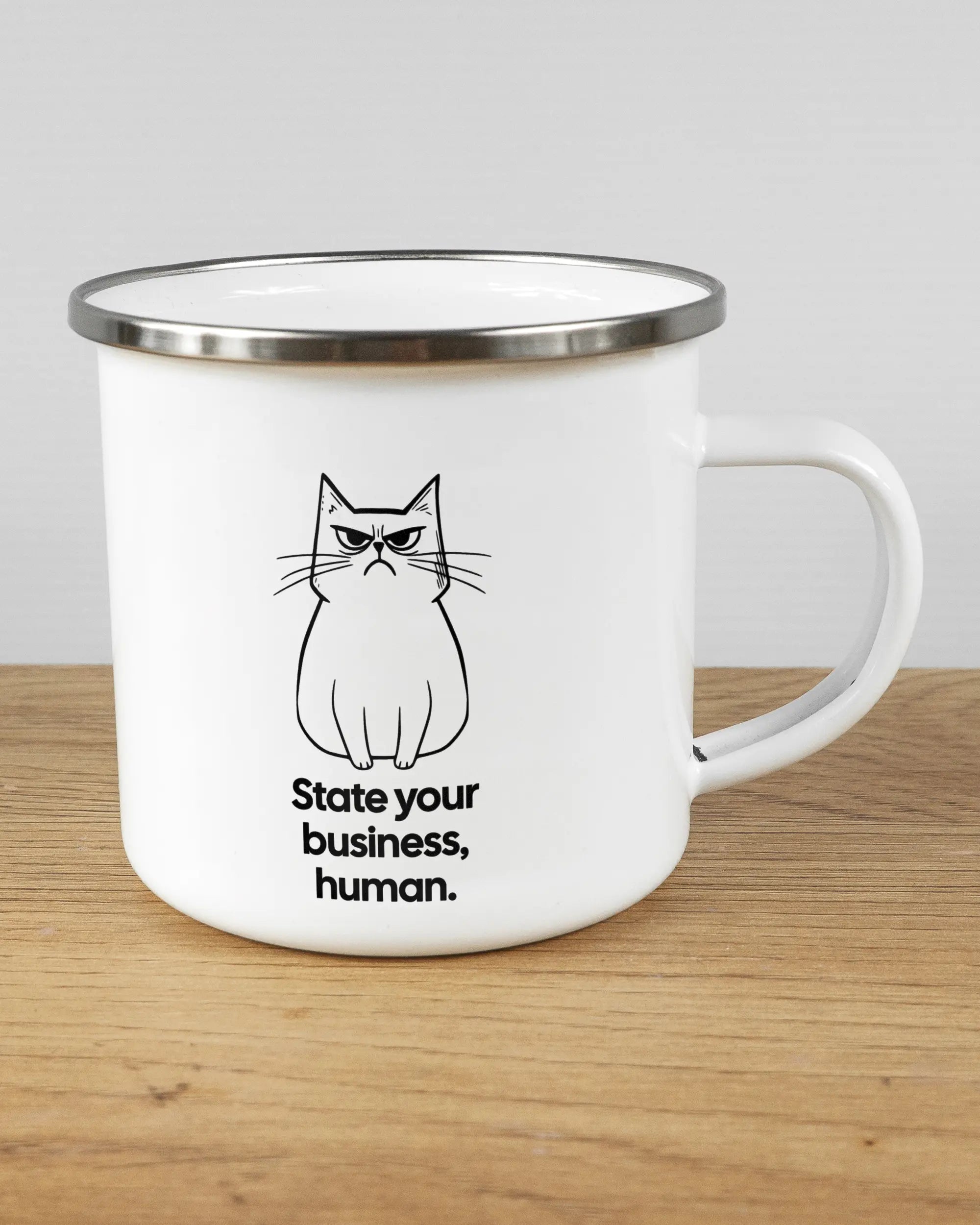 Alternativbild, das die rechte Seite der beidseitig bedruckten Emailletasse von Maondo mit dem Design Grumpy Purr in der Farbe White-Silver auf einem Holztisch zeigt