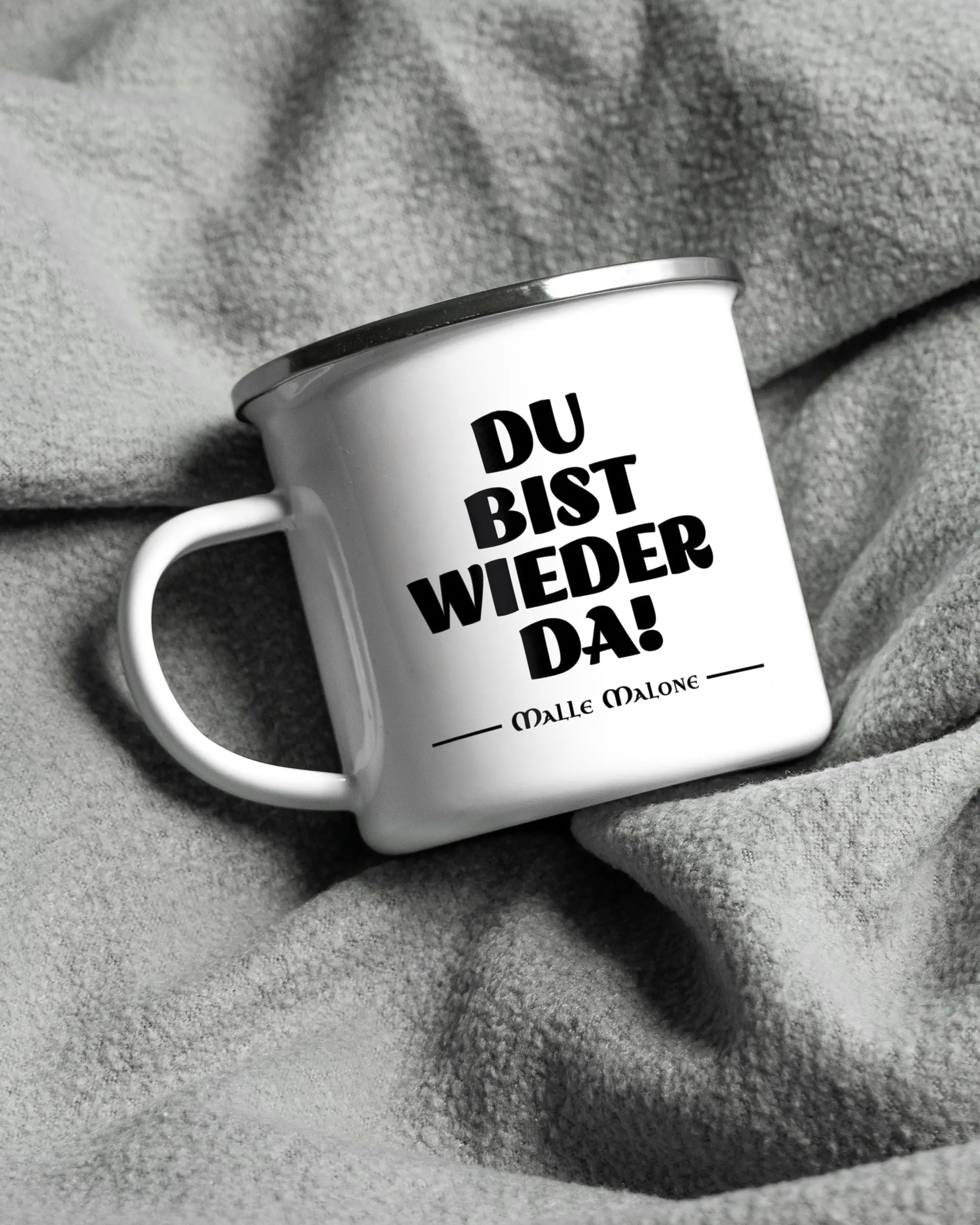 Aufnahme, die die linke Seite der beidseitig bedruckten Emailletasse von Maondo auf einer flauschigen Fließdecke mit dem Design White-Silver in der Farbe  zeigt