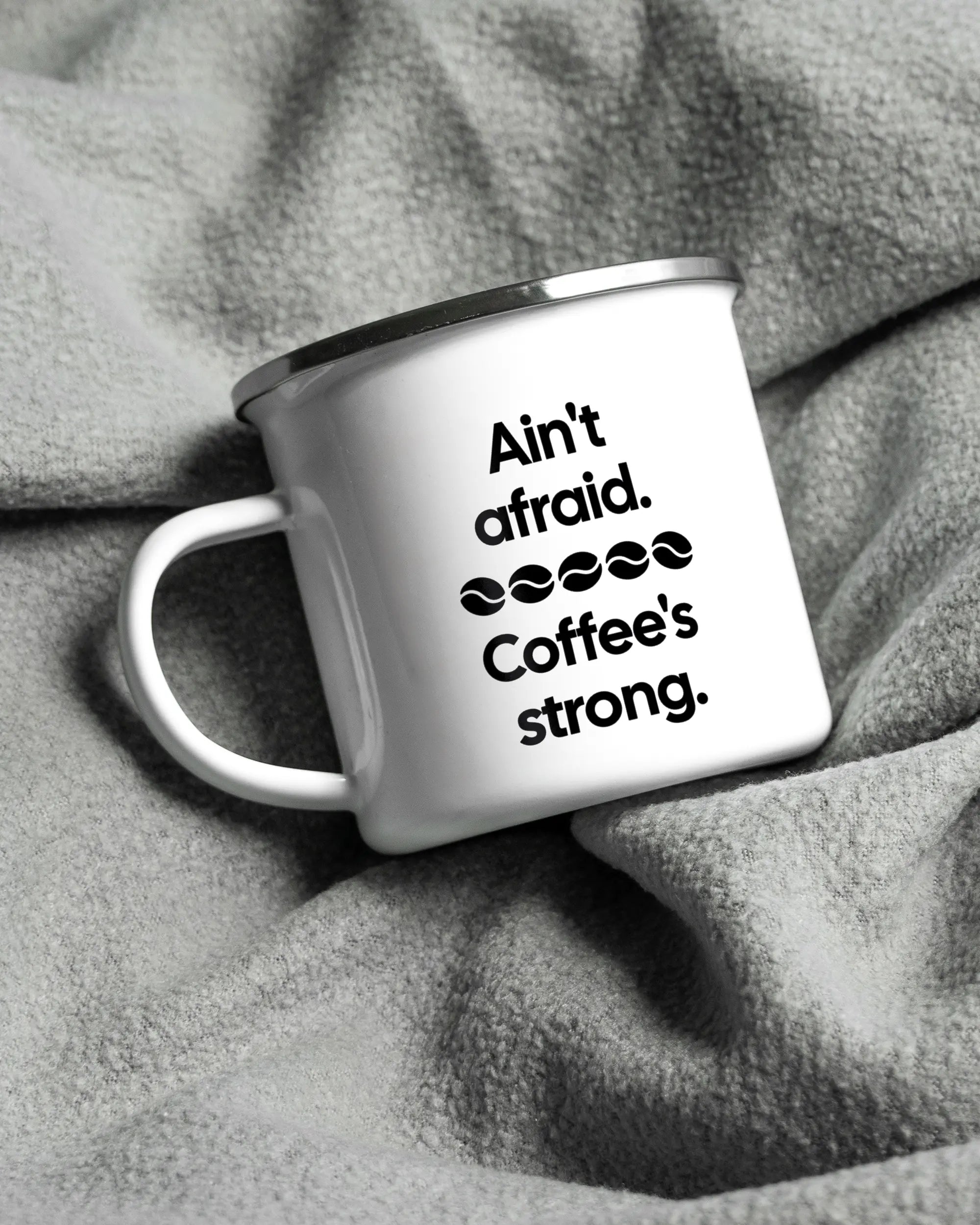 Aufnahme, die die linke Seite der beidseitig bedruckten Emailletasse von Maondo auf einer flauschigen Fließdecke mit dem Design White-Silver in der Farbe  zeigt