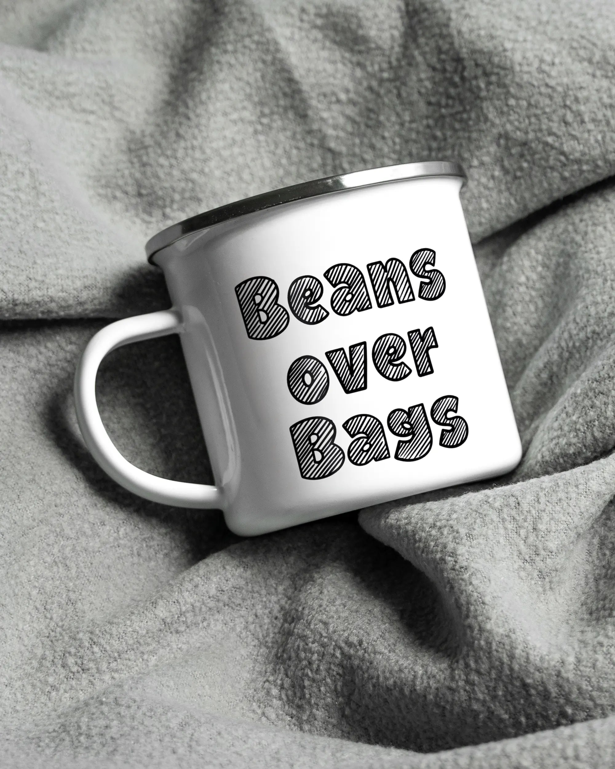 Aufnahme, die die linke Seite der beidseitig bedruckten Emailletasse von Maondo auf einer flauschigen Fließdecke mit dem Design White-Silver in der Farbe  zeigt