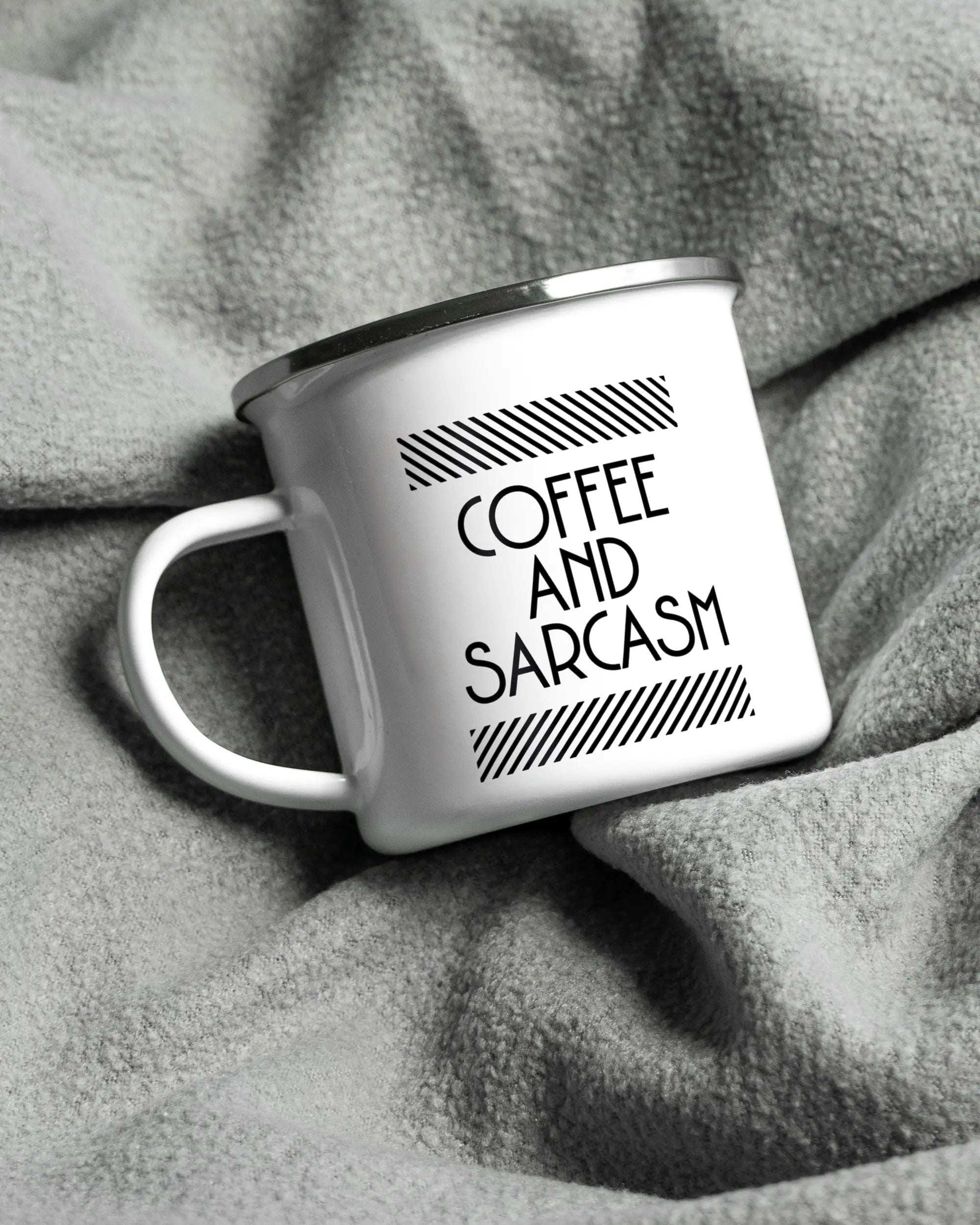 Aufnahme, die die linke Seite der beidseitig bedruckten Emailletasse von Maondo auf einer flauschigen Fließdecke mit dem Design White-Silver in der Farbe  zeigt