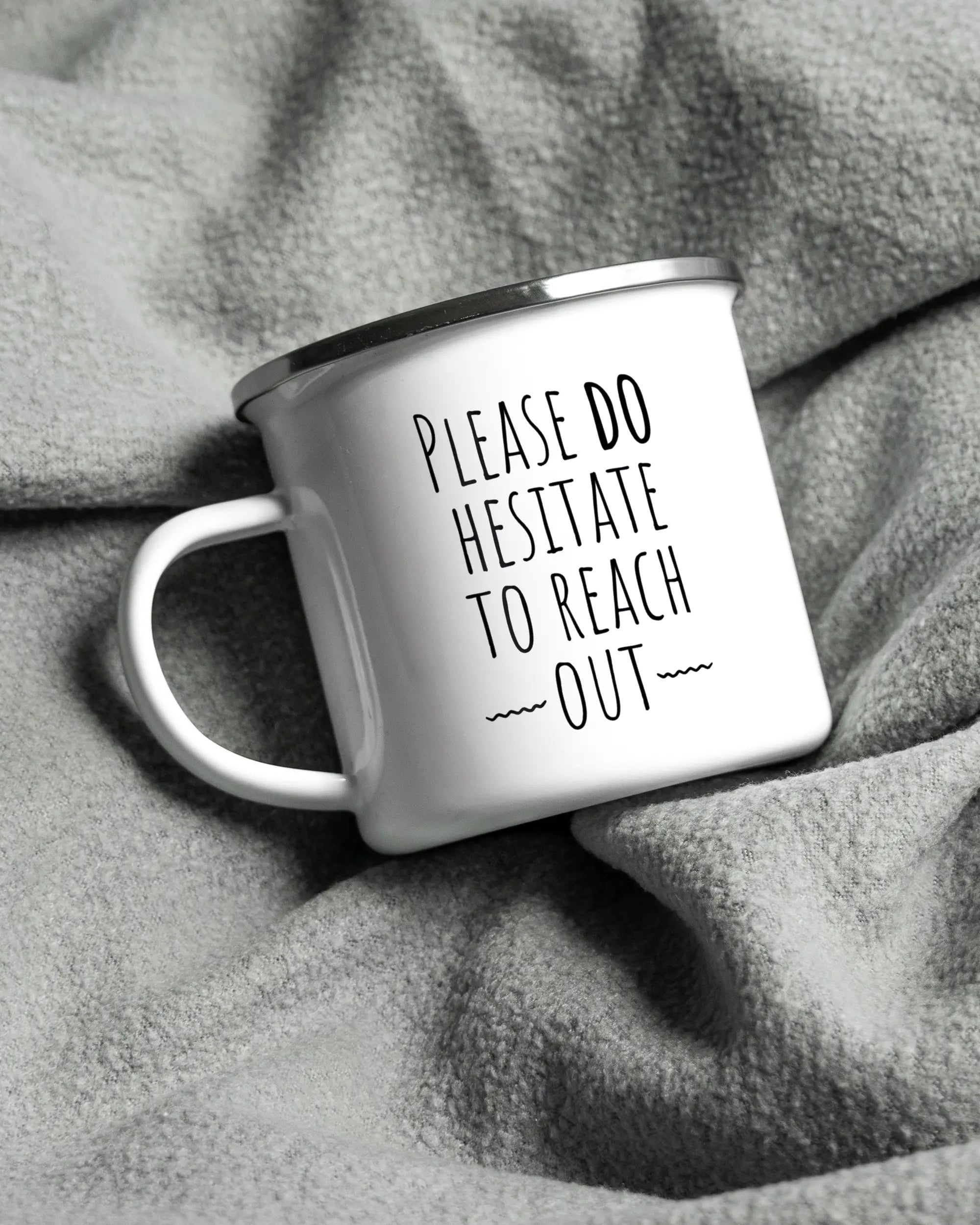 Aufnahme, die die linke Seite der beidseitig bedruckten Emailletasse von Maondo auf einer flauschigen Fließdecke mit dem Design White-Silver in der Farbe  zeigt