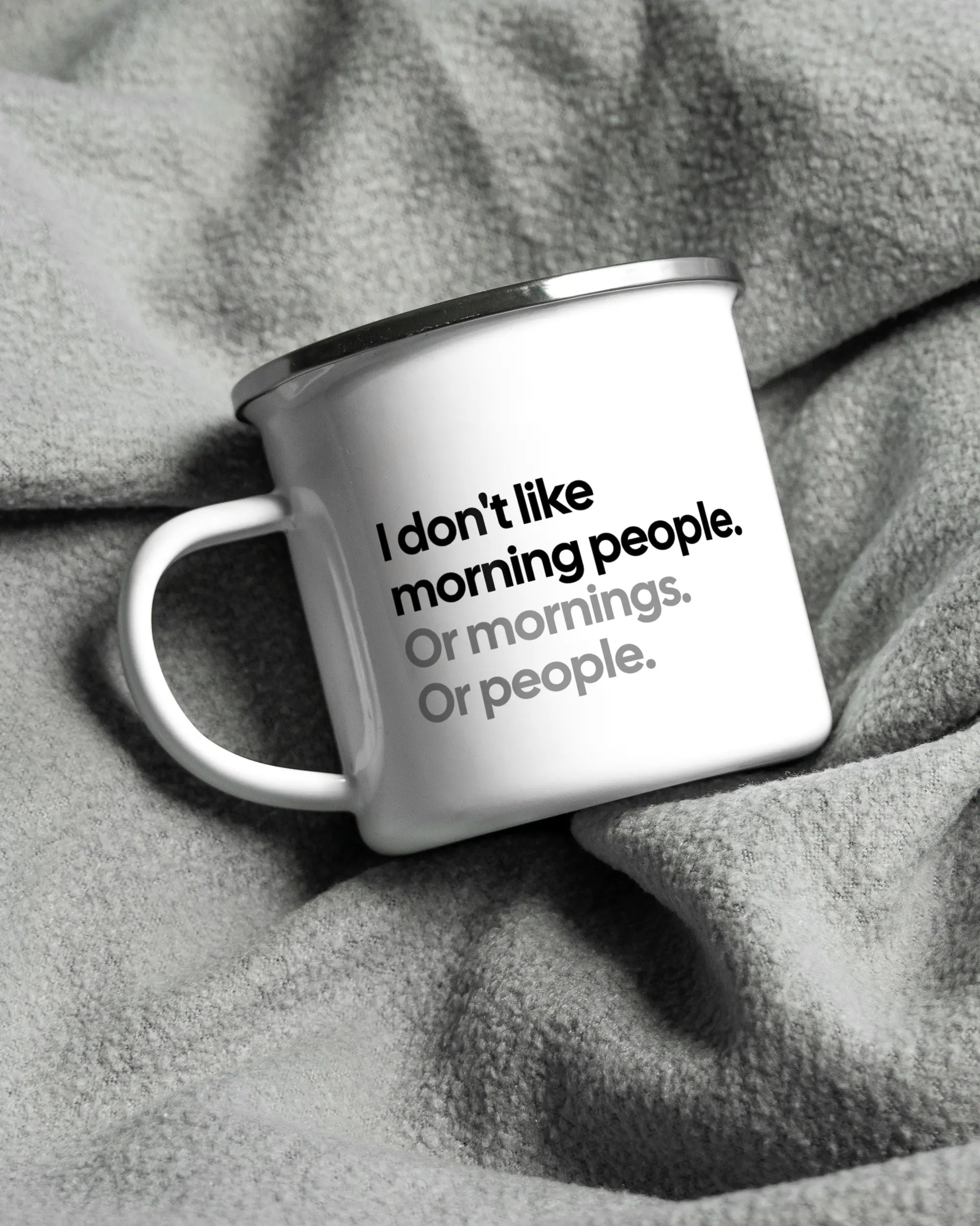 Aufnahme, die die linke Seite der beidseitig bedruckten Emailletasse von Maondo auf einer flauschigen Fließdecke mit dem Design White-Silver in der Farbe  zeigt