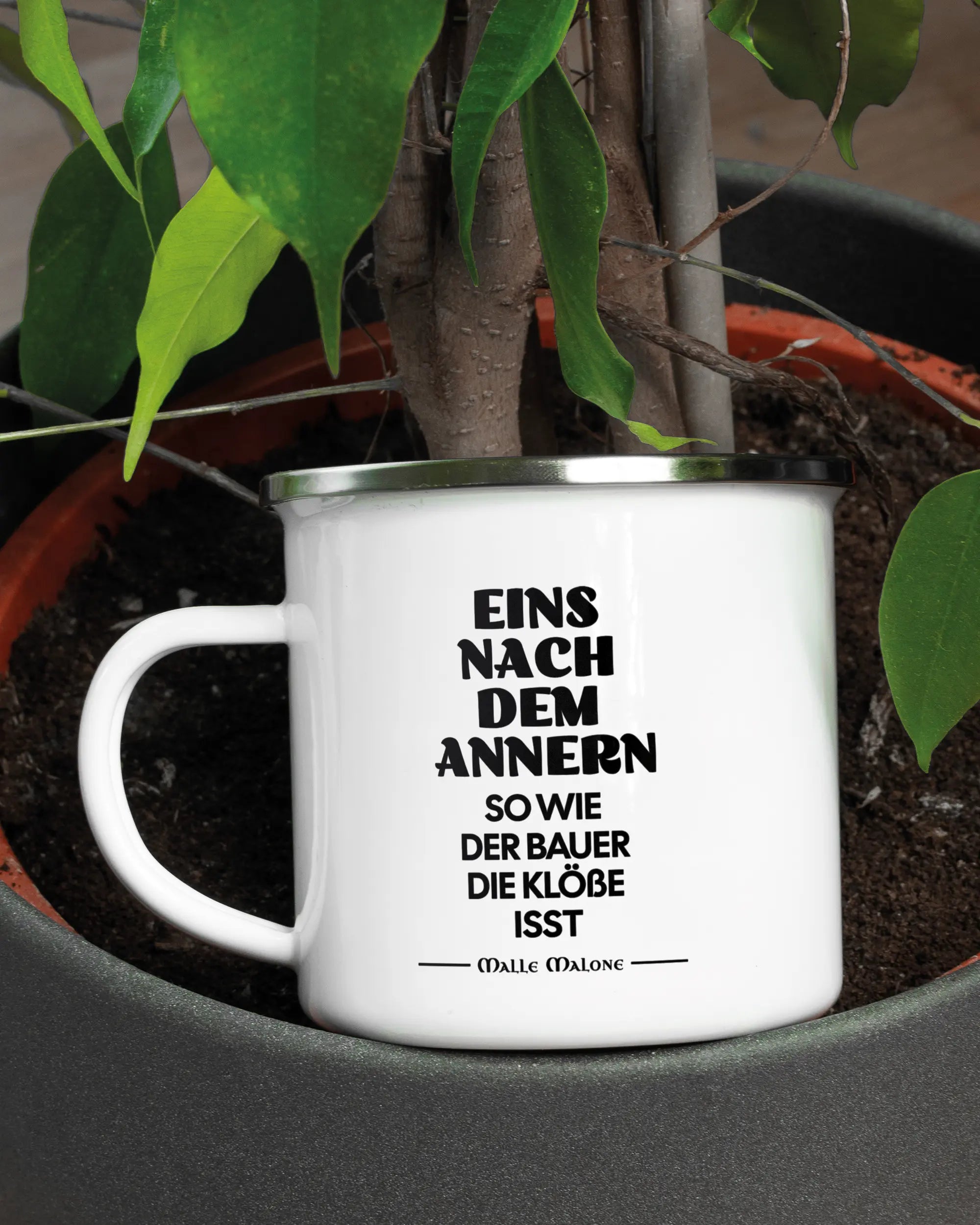 Aufnahme der linken Seite der beidseitig bedruckten Emailletasse von Maondo mit dem Design Eins nach dem Annern in der Farbe White-Silver in einem Blumentopf