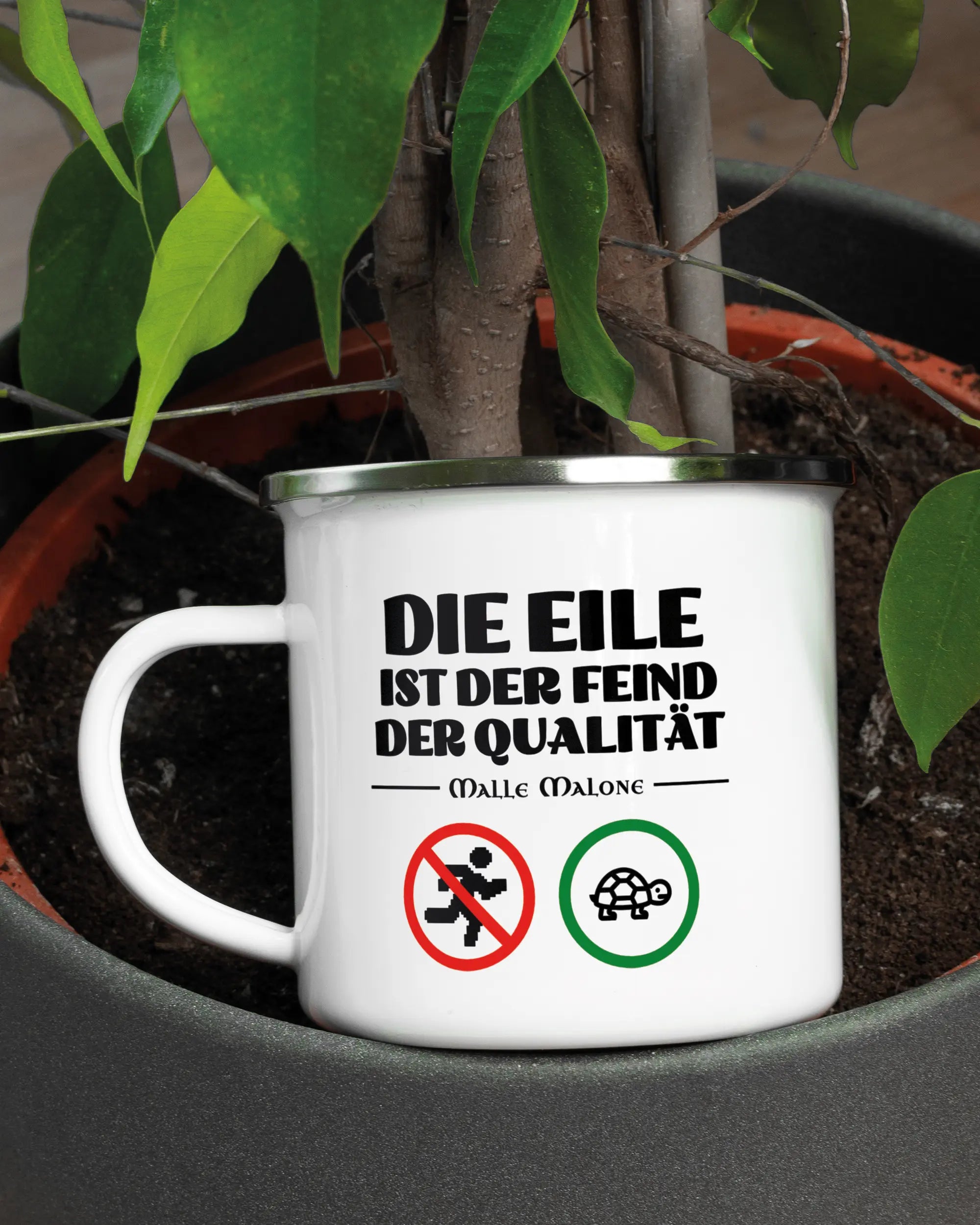 Aufnahme der linken Seite der beidseitig bedruckten Emailletasse von Maondo mit dem Design Keine Eile in der Farbe White-Silver in einem Blumentopf