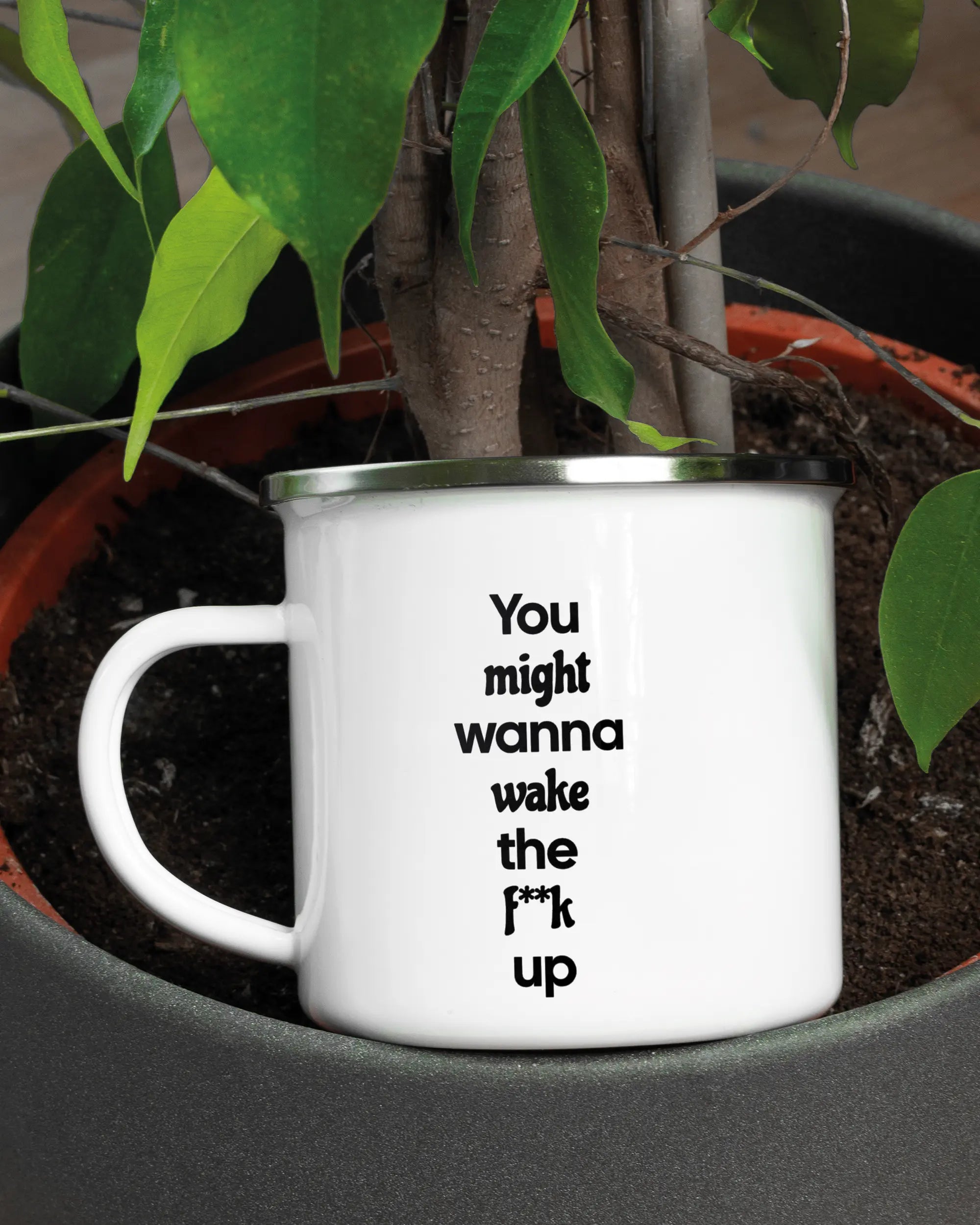 Aufnahme der linken Seite der beidseitig bedruckten Emailletasse von Maondo mit dem Design Wanna Wake in der Farbe White-Silver in einem Blumentopf