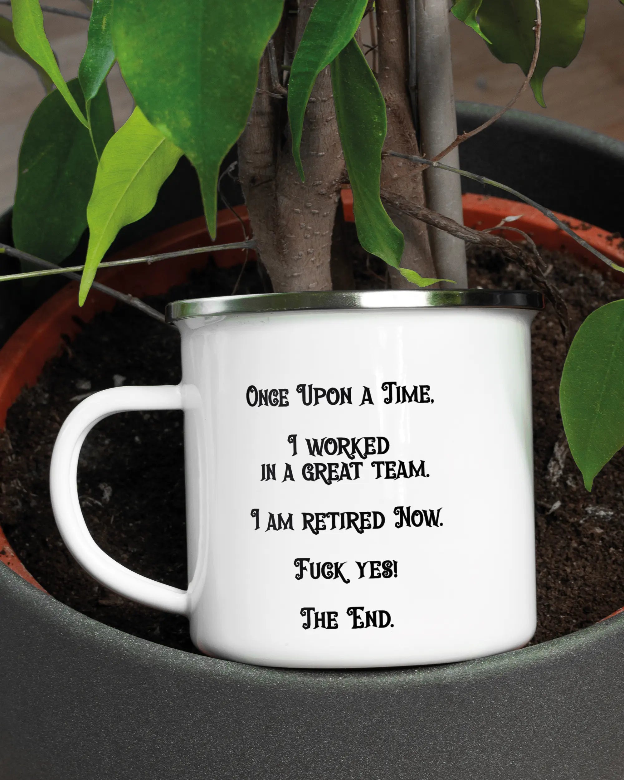 Aufnahme der linken Seite der beidseitig bedruckten Emailletasse von Maondo mit dem Design Finally Retired in der Farbe White-Silver in einem Blumentopf