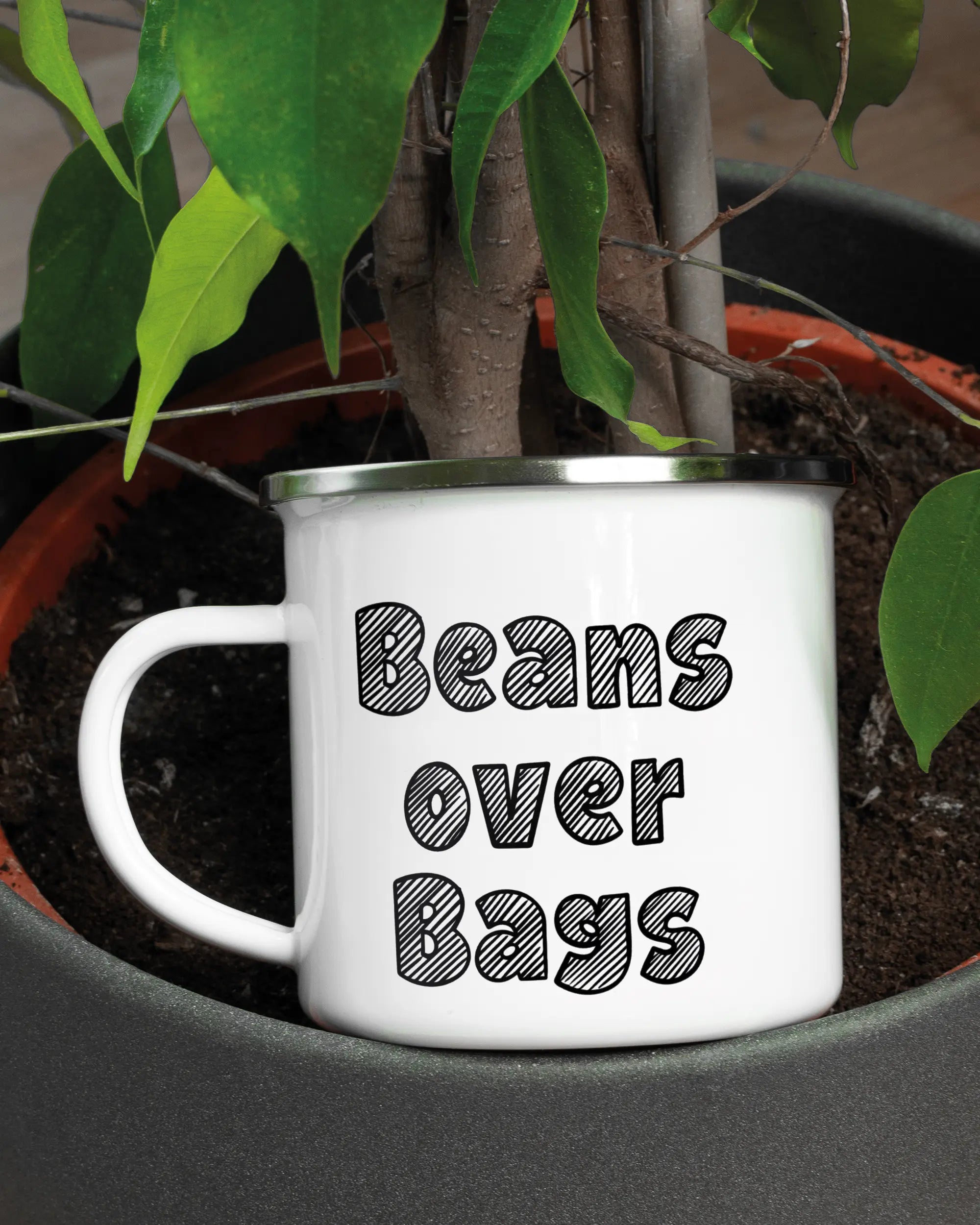 Aufnahme der linken Seite der beidseitig bedruckten Emailletasse von Maondo mit dem Design Beans over Bags in der Farbe White-Silver in einem Blumentopf