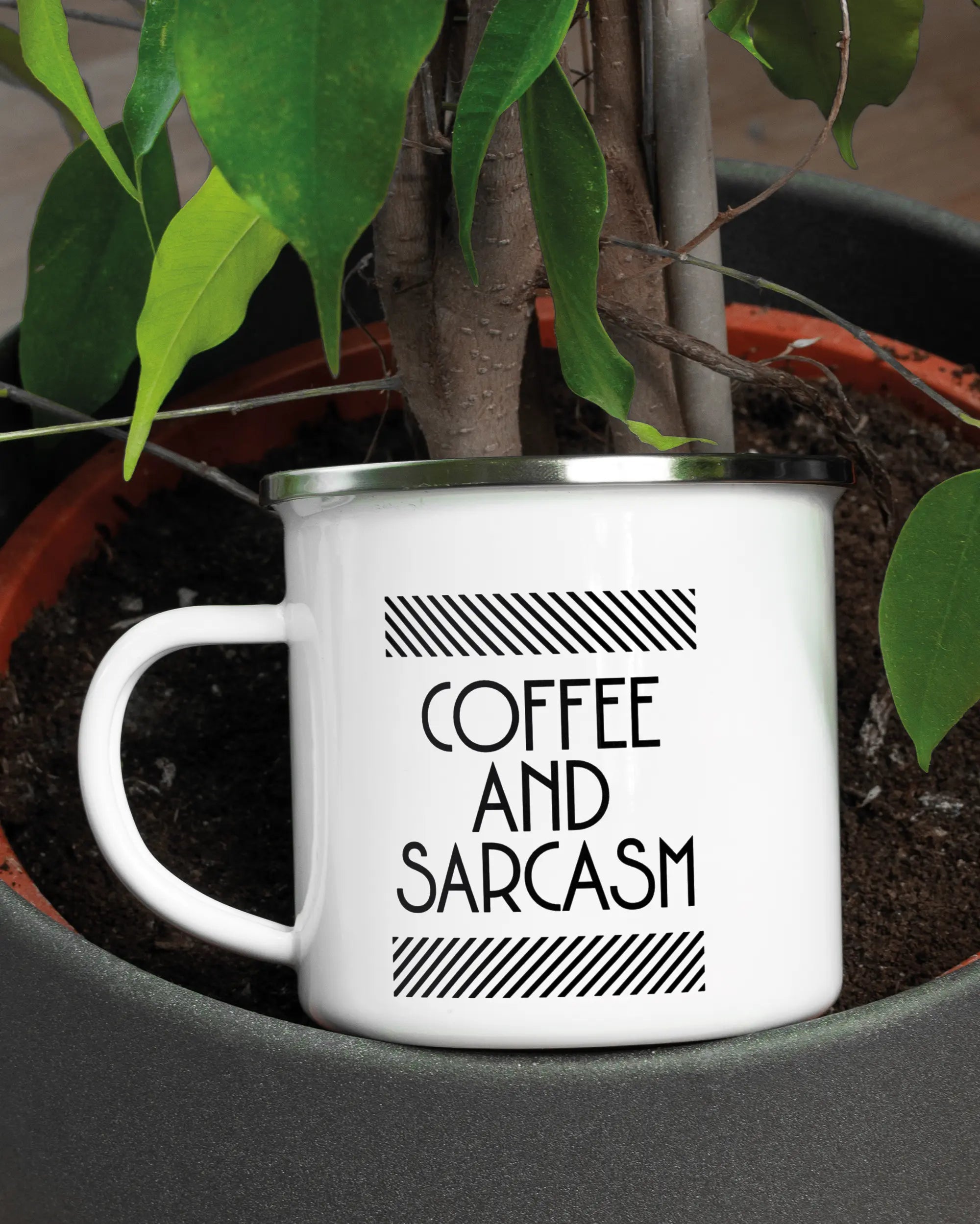 Aufnahme der linken Seite der beidseitig bedruckten Emailletasse von Maondo mit dem Design Sarcastic Cup in der Farbe White-Silver in einem Blumentopf