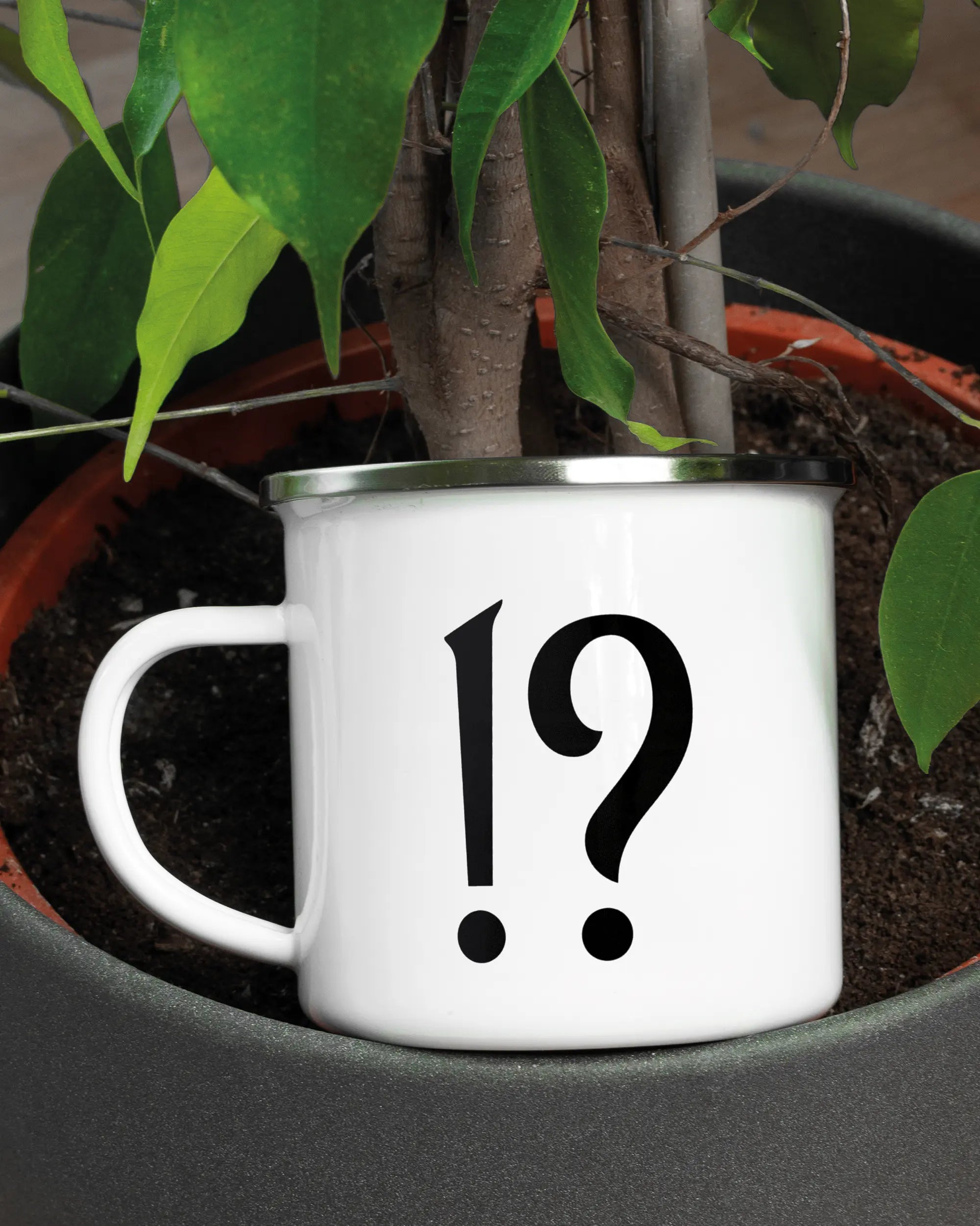 Aufnahme der linken Seite der beidseitig bedruckten Emailletasse von Maondo mit dem Design WHAT in der Farbe White-Silver in einem Blumentopf