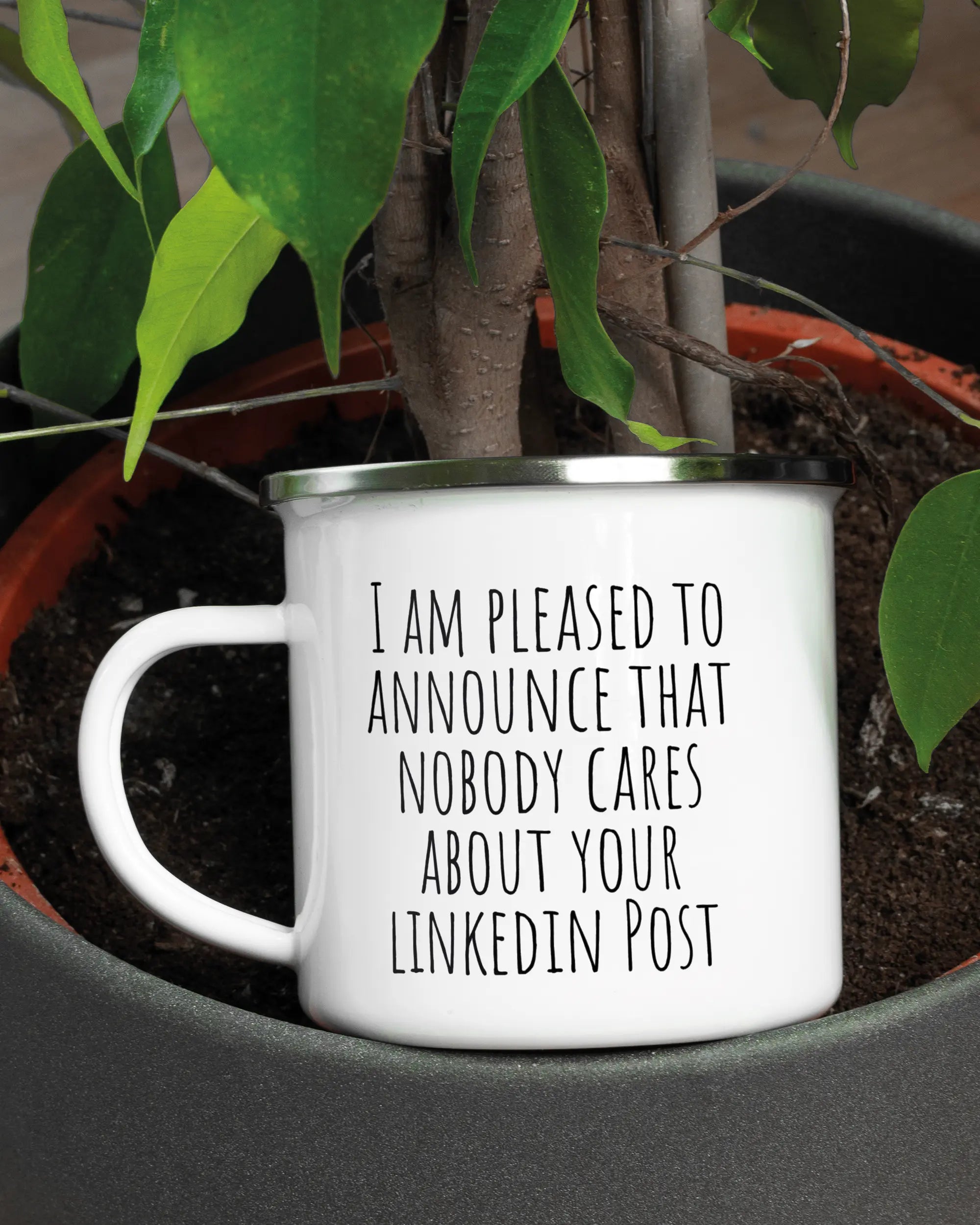 Aufnahme der linken Seite der beidseitig bedruckten Emailletasse von Maondo mit dem Design Please Unannounce in der Farbe White-Silver in einem Blumentopf