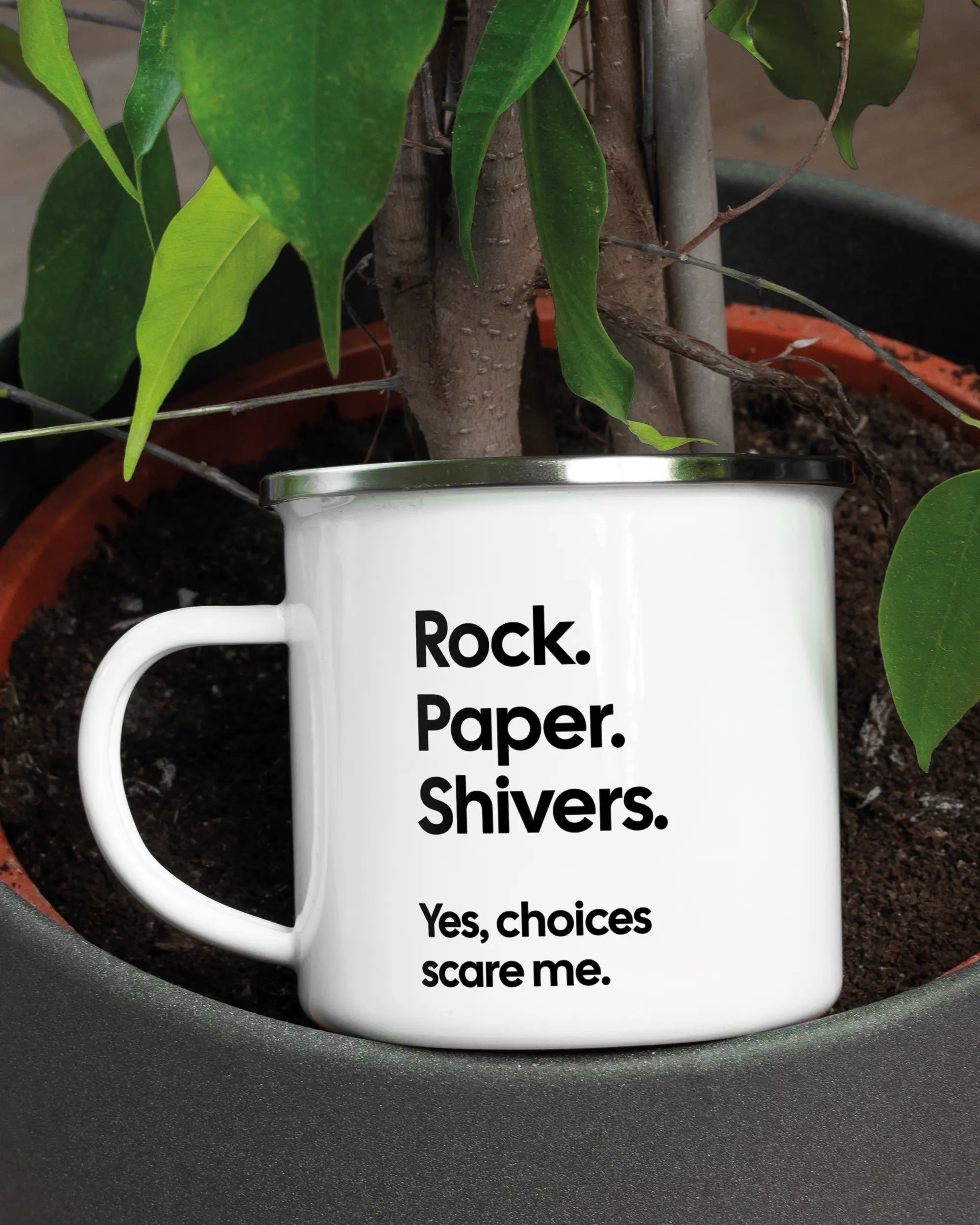 Aufnahme der linken Seite der beidseitig bedruckten Emailletasse von Maondo mit dem Design Rock Paper Shivers in der Farbe White-Silver in einem Blumentopf