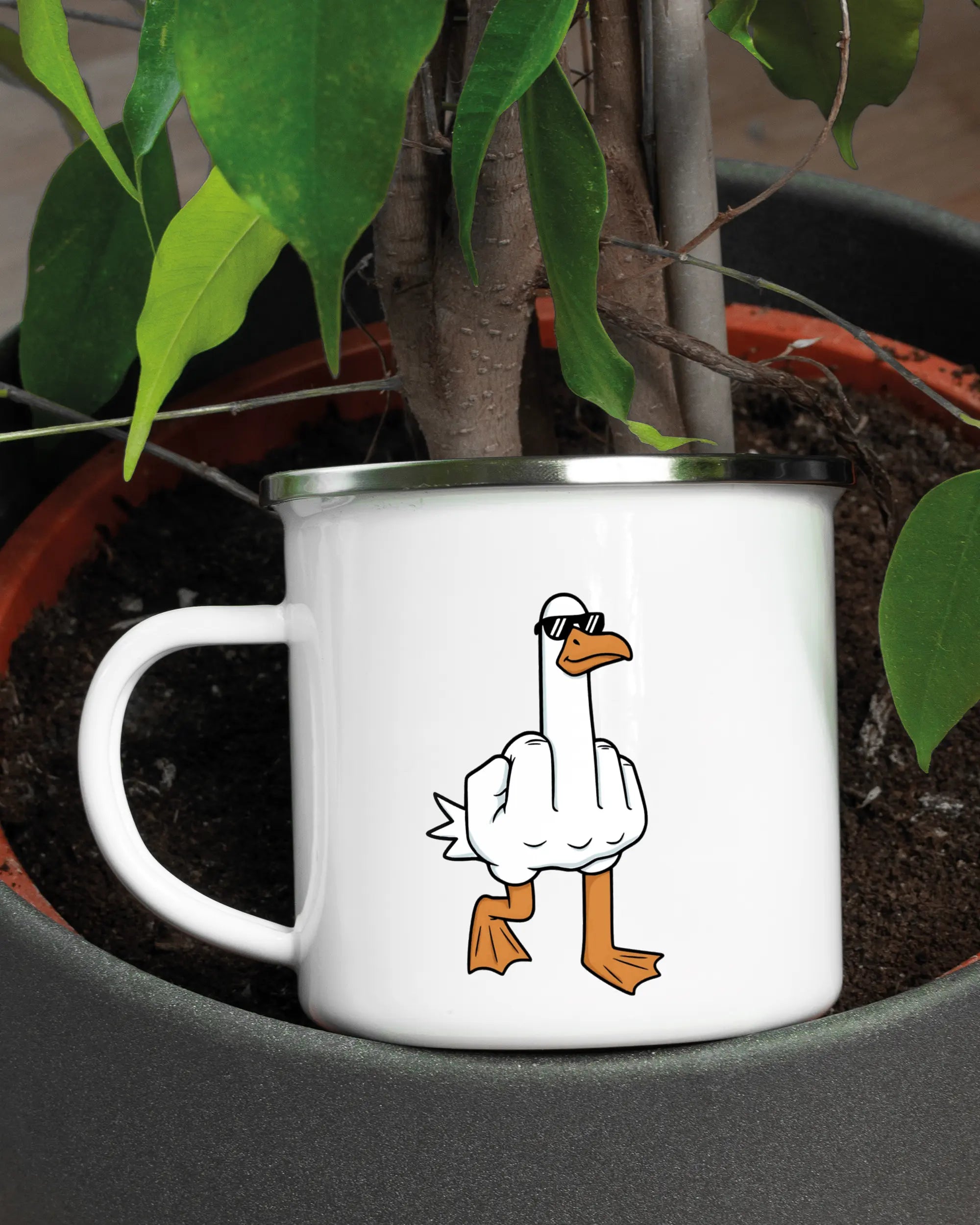 Aufnahme der linken Seite der beidseitig bedruckten Emailletasse von Maondo mit dem Design I give a duck in der Farbe White-Silver in einem Blumentopf
