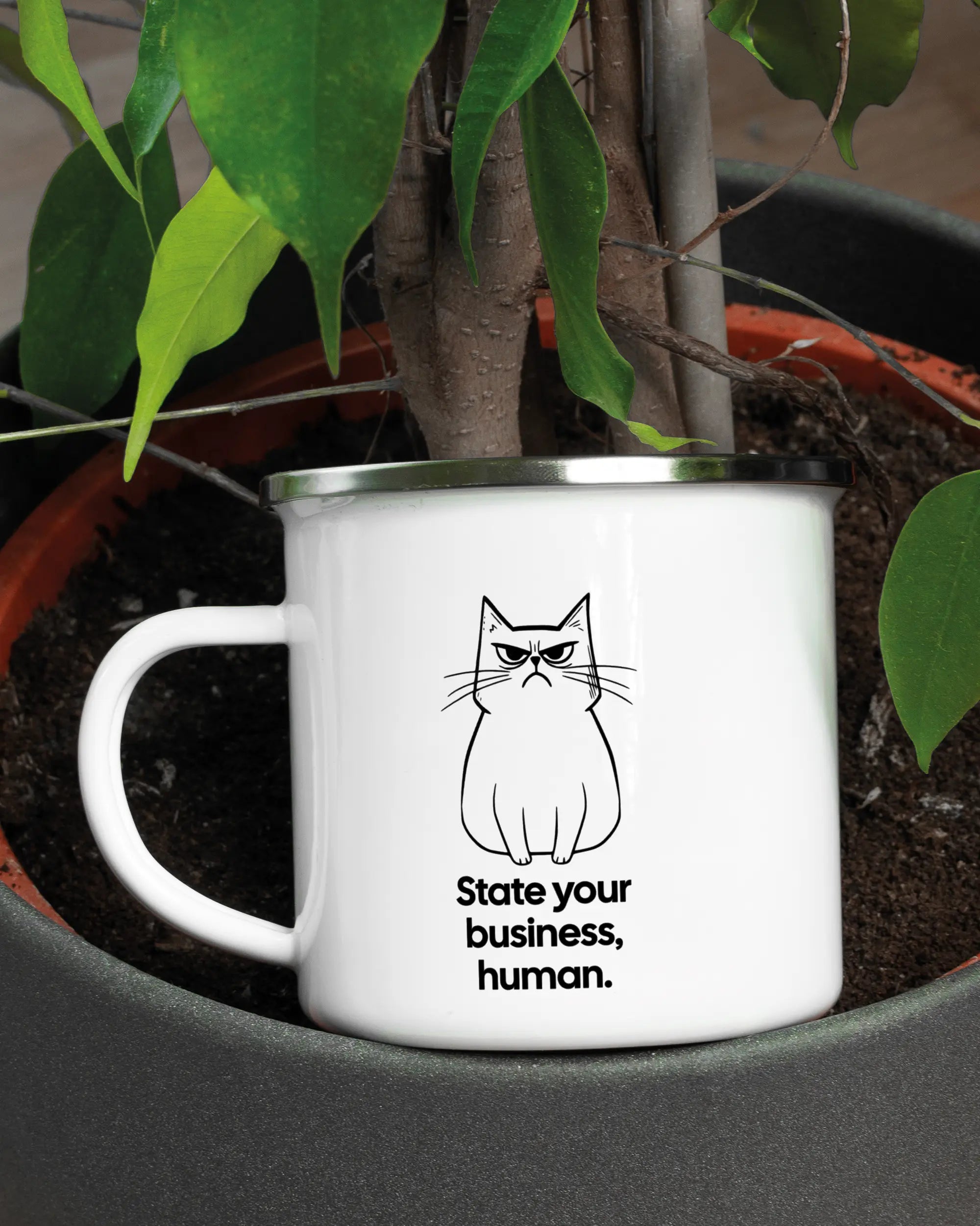 Aufnahme der linken Seite der beidseitig bedruckten Emailletasse von Maondo mit dem Design Grumpy Purr in der Farbe White-Silver in einem Blumentopf