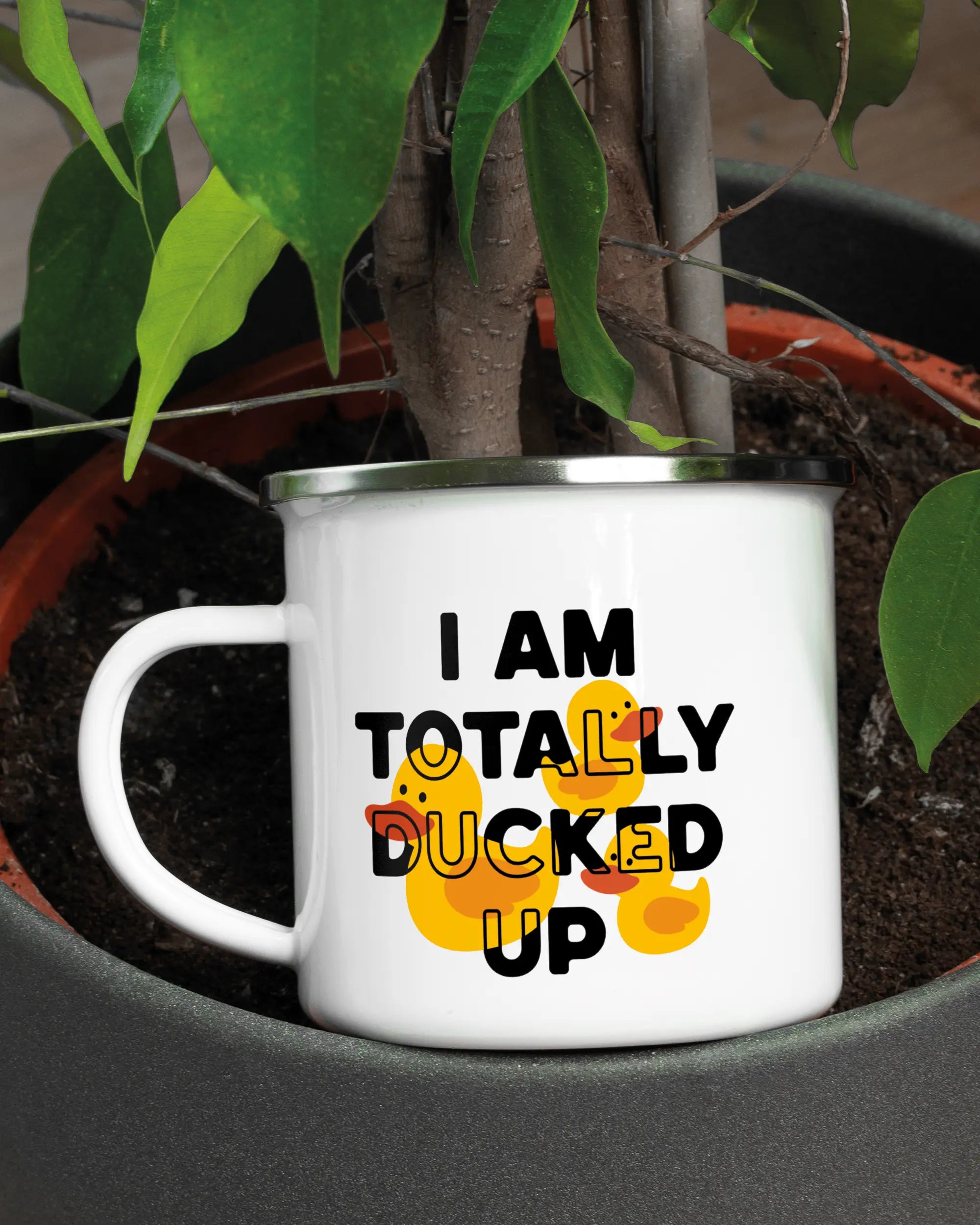 Aufnahme der linken Seite der beidseitig bedruckten Emailletasse von Maondo mit dem Design Ducked Up in der Farbe White-Silver in einem Blumentopf