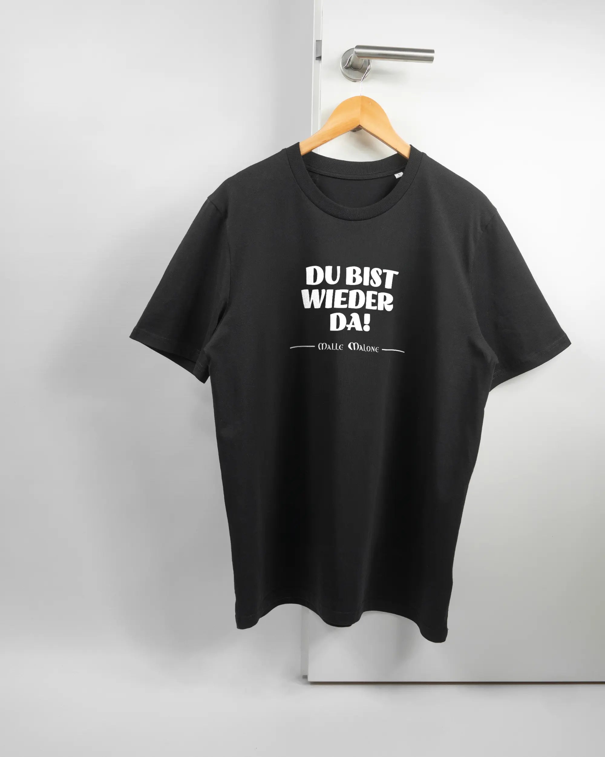 Vorderseite des Organic Unisex T-Shirt Casual von Maondo mit dem Design Wieder da in der Farbe Black und in der Größe L auf einem Bügel an der Türklinke aufgehängt